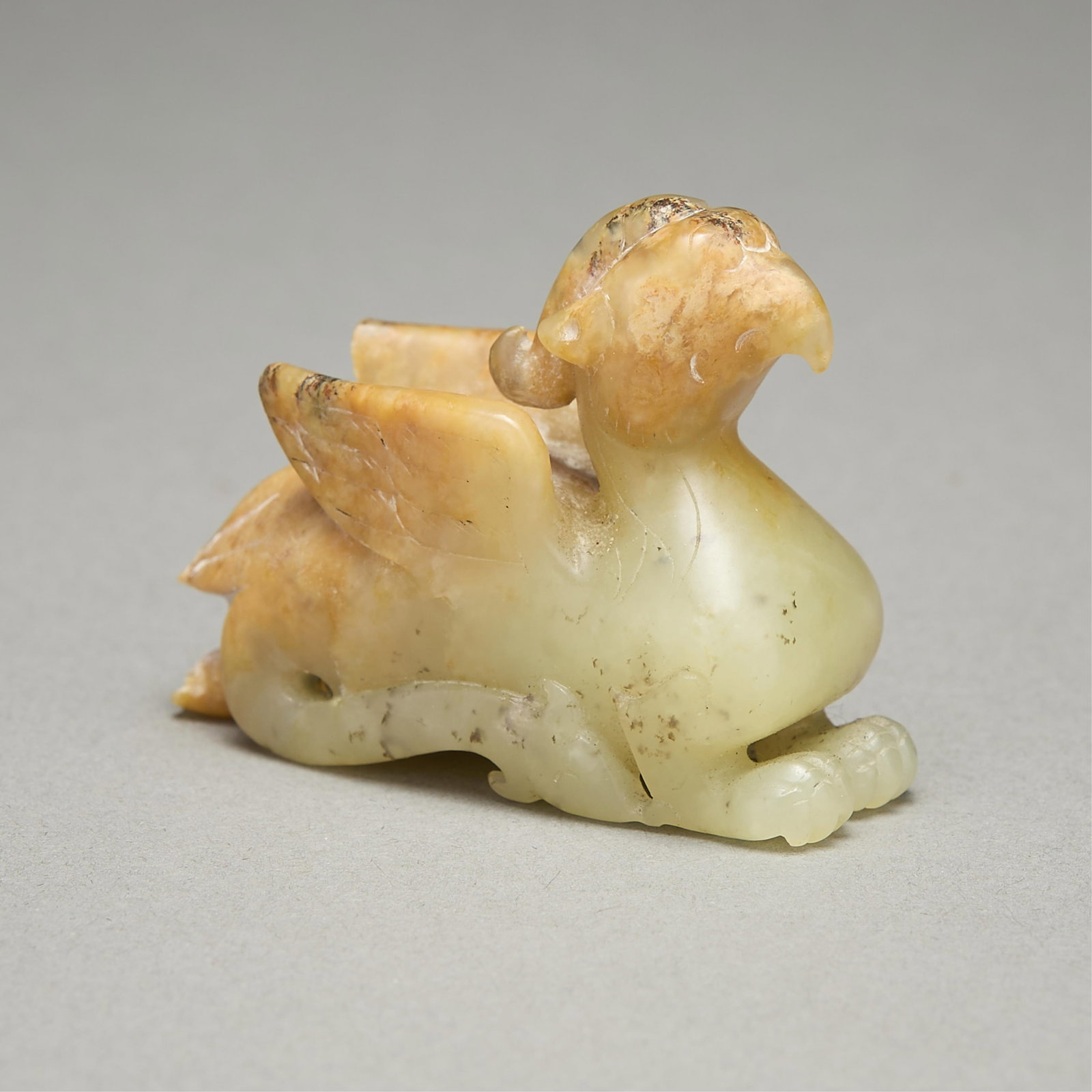 Chinese Carved Jade Gryphon Bead: Chinese carved jade mythical gryphon or griffin bird figure bead. The chest and lower body of pale green jade; the head and wings skillfully carved to the contours of the stone's russet inclusions. Li