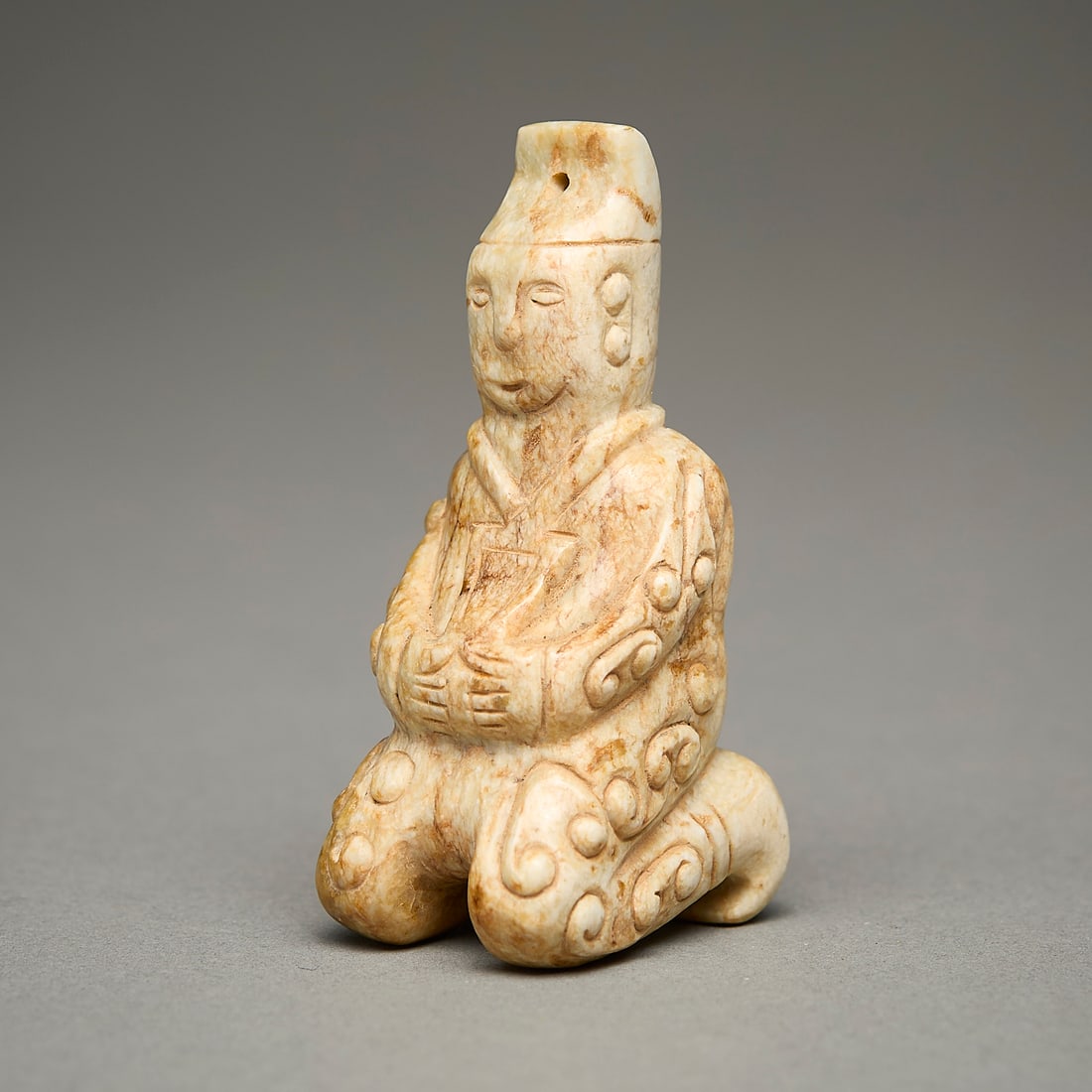Chinese Carved Jade or Hardstone Kneeling Figure: Chinese carved jade or hardstone kneeling male figure yupei pendant. With intricate incised scrollwork motifs.Height: 2 1/4 in x width: 1 in x depth: 1 1/4 in.