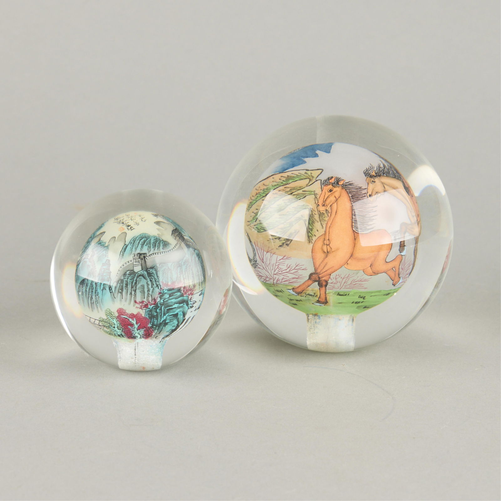 2 Chinese Glass Ball Paper Weights: Group of two Chinese glass paper weights of spherical form. One depicting the Great Wall of China, and the other featuring wild horses.(Larger) Height: 4 in x diameter: 4 1/2 in. (Smaller) Height: 3 i