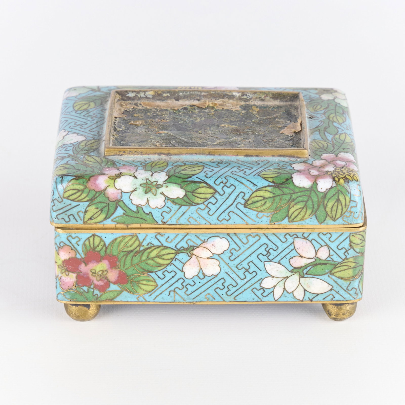 Small Blue Chinese Cloisonne Floral Trinket Box: Small Chinese cloisonne trinket box with hinged lid. Depicting floral motifs on light blue ground. Supported atop ball form feet.Height: 1 1/2 in x width: 3 1/2 in x depth: 3 in.