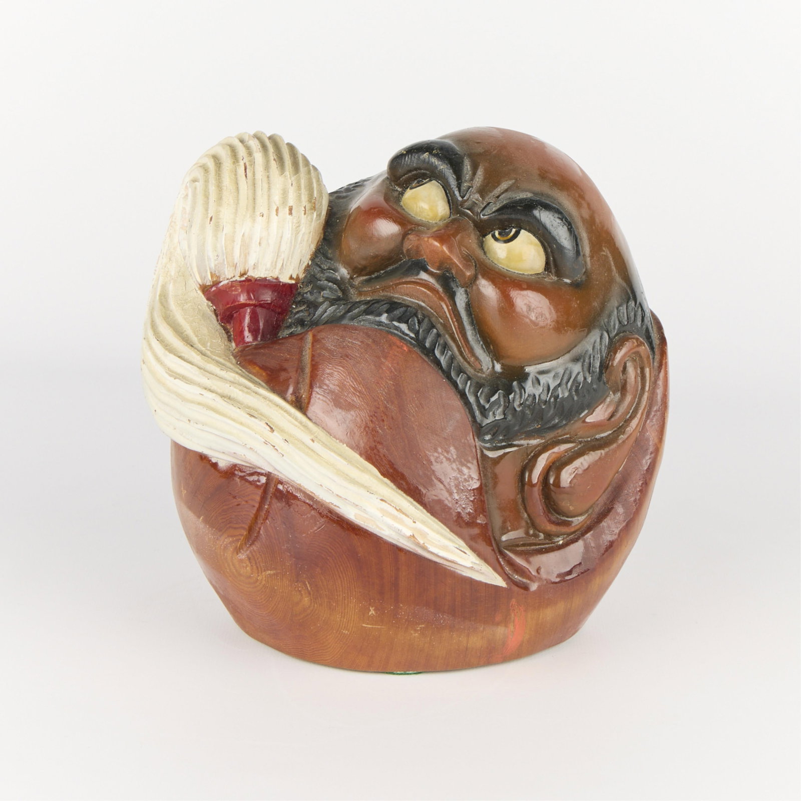 Japanese Carved Wooden Daruma Figurine: Japanese carved wooden Daruma figurine depicting the head of a bearded man holding a long paintbrush. Height: 7 1/2 in x width: 8 in x depth: 7 in.
