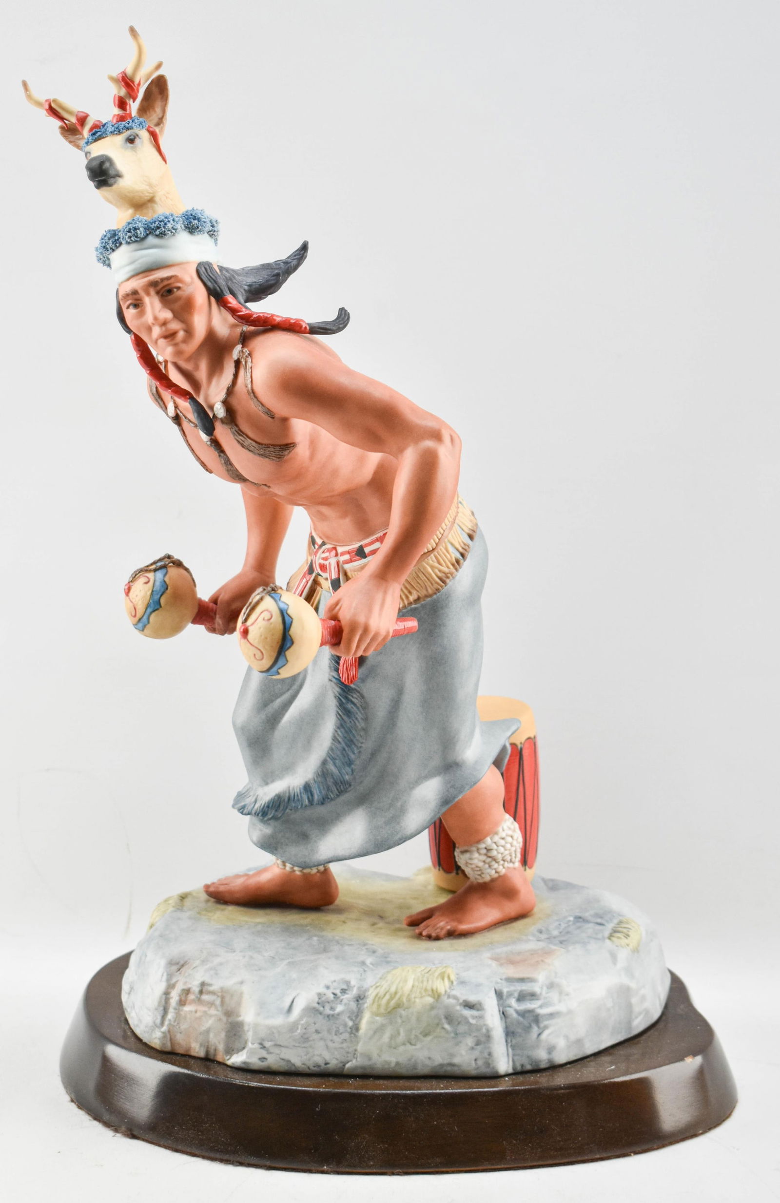 Cybis Porcelain Yaqui Deer Dancer Sculpture: Vintage hand painted porcelain sculpture by Cybis Porcelain depicting a Yaqui dancer wearing a deer horn headdress over long black hair, a blue fringed kilt, and white shells are wrapped around his an