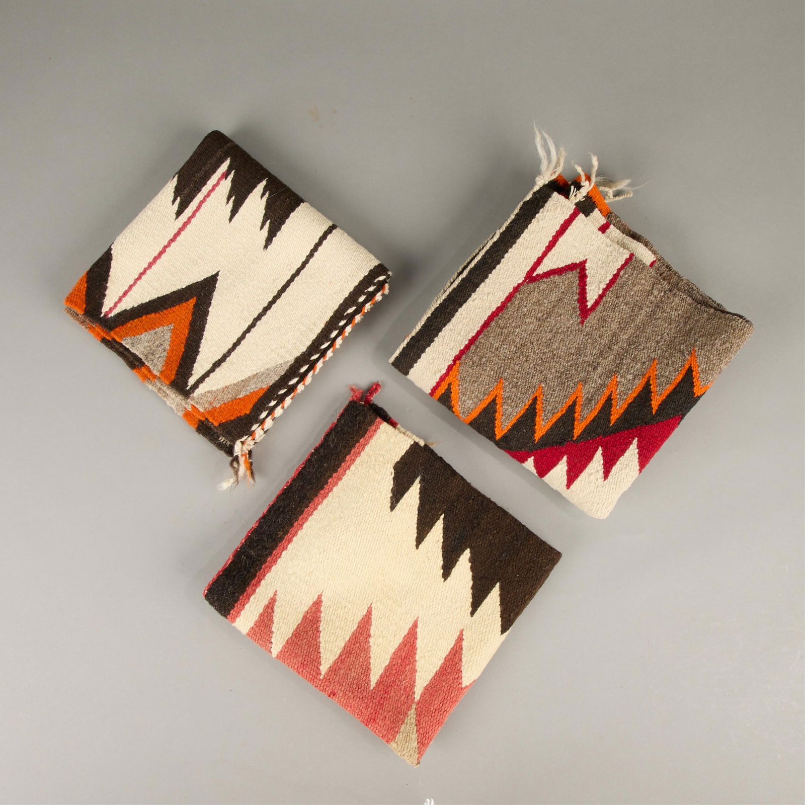3 Southwestern Navajo Wool Saddle Blanket Textiles: Group of three Dine (Navajo) wool rug or saddle blanket textiles, 19th-20th century. Including:One saddle blanket with serrated central diamond motif. Executed in red and black against a cream ground.
