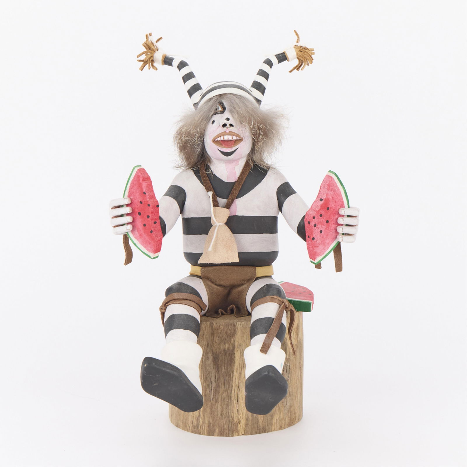 M. Cleveland "Hand Clown" Kachina Doll: Hopi wooden polychrome katsina sculpture depicting a clown eating watermelon. Mounted atop a wood base. Signed and titled along the underside.Height: 8 1/2 in x width: 5 1/2 in x depth: 6 in.