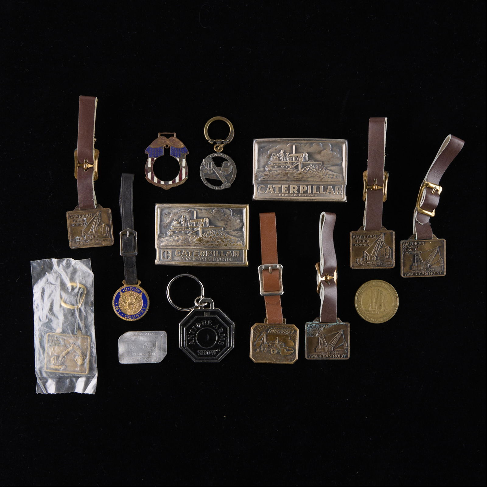 14 Assorted Watch Fobs, Belt Buckles, & More: Group of 14 assorted vintage watch fobs, belt buckles, advertising souvenirs, keychains, and militaria. Including items from Caterpillar Inc., American Hoist, Antique Arms Show, and more! (Shipping