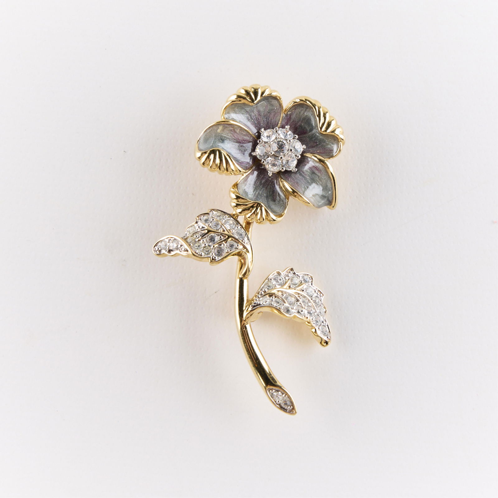 Nolan Miller Glamour Collection Flower Brooch: Nolan Miller gold-toned flower brooch. Depicting a blooming grey or light purple enamel flower, decorated with clear rhinestones. From the Nolan Miller Glamour Collection. Maker's marks along the