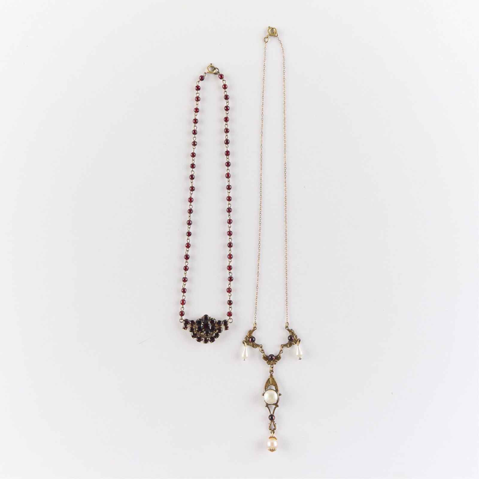 2 Costume Necklaces: Group two costume jewelry necklaces of antique style lavalier and swag form with red stones and faux pearls. Length ranges from 16 in to 19 in. Gross weight: 15.2 g.