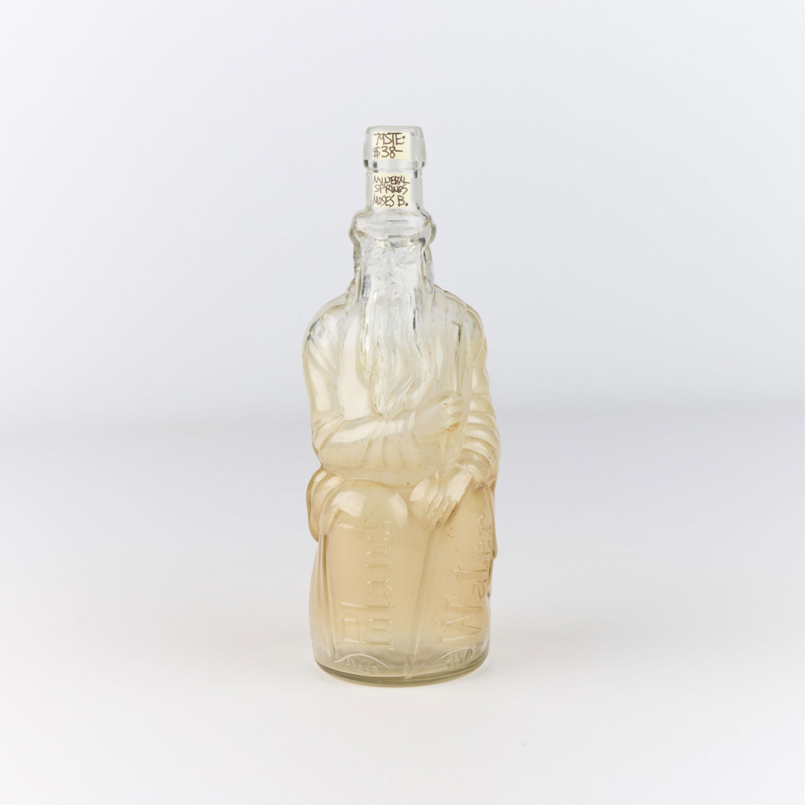 Poland Mineral Water Co. "Moses" Glass Bottle: Poland Spring Company glass commemorative mineral water "Moses" bottle, ca. 20th century. Depicting a seated biblical figure, possibly holding the Ten Commandments. Impressed mark along the back of th