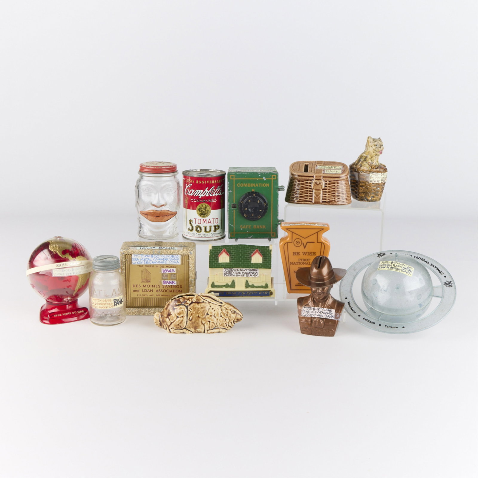 12 Vintage Regional & International Coin Banks: Group of 12 vintage regional and international advertising coin banks. Including Norwegian Skjeberg Savings coin bank, Des Moines Savings and Loan coin bank, and ten additional banks.Height ranges fro