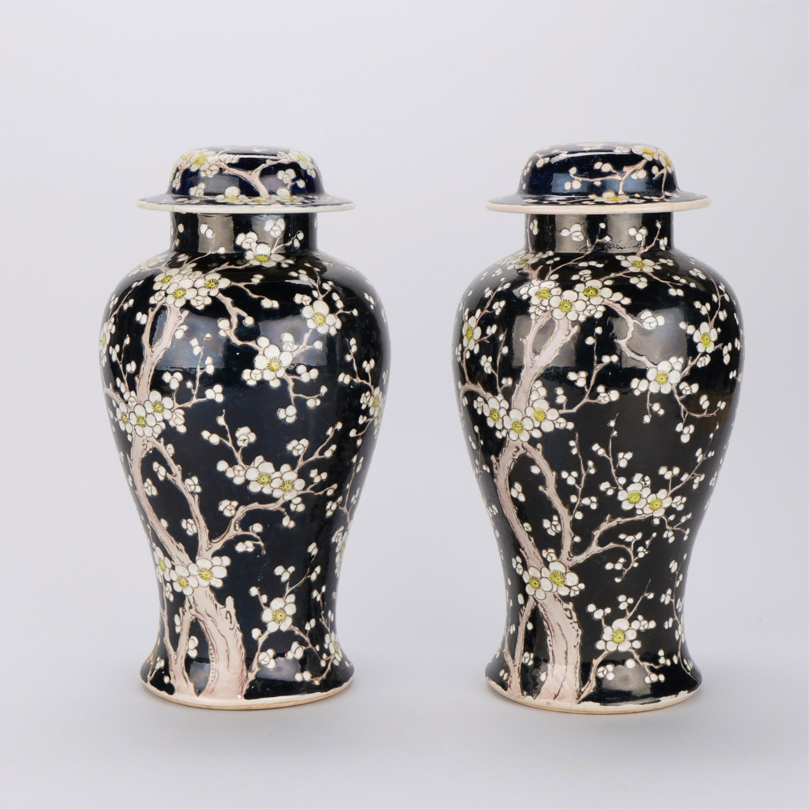 Pr Japanese Porcelain White Prunus Vases: Pair of Japanese porcelain lidded baluster vases depicting white prunus plum or cherry blossom motifs on black ground. One vase with a paper label affixed along the underside; numbered 662 along the l