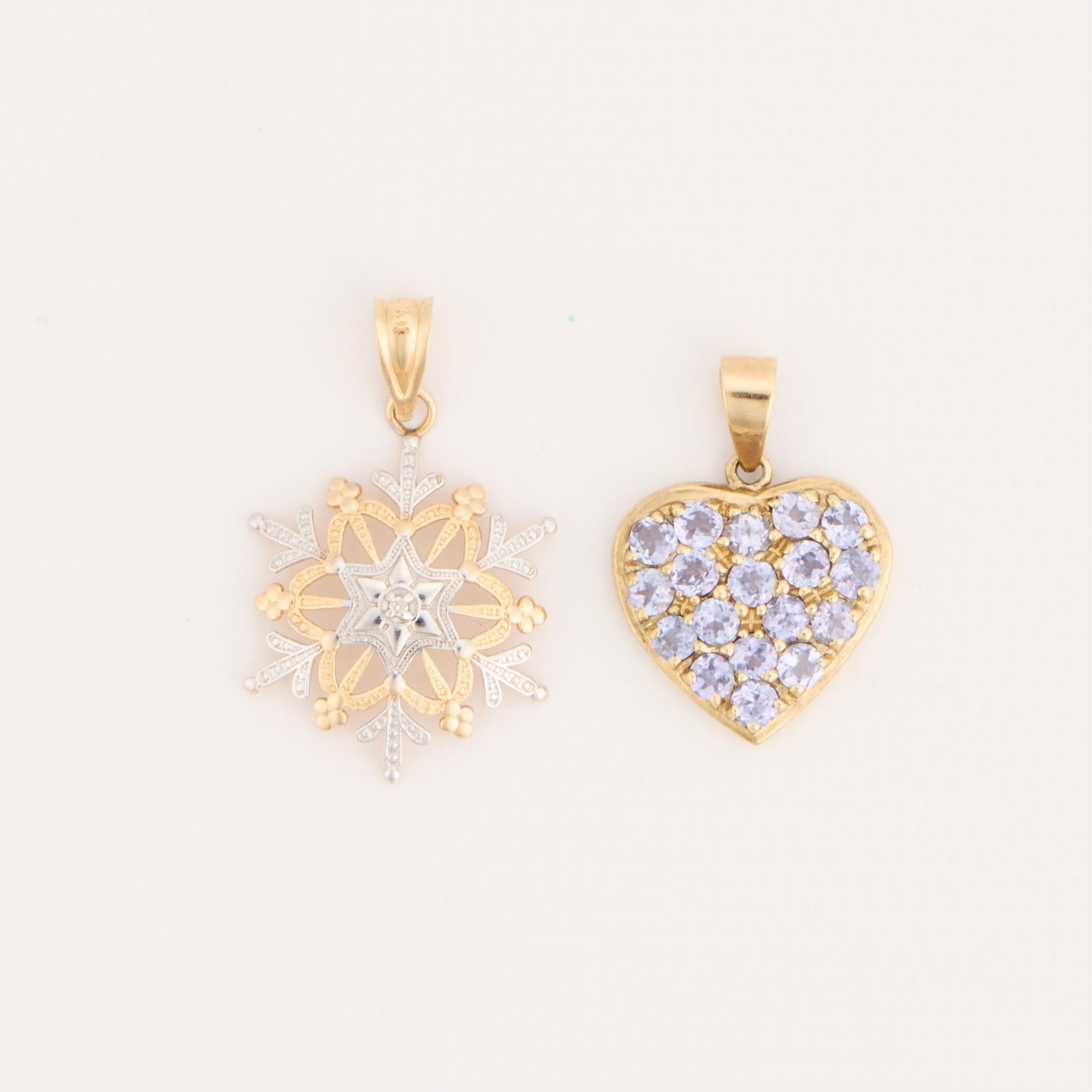 Michael Anthony 14k Gold & Trifari 10k Gold Pendants: Group of two gold pendants. Including one Michael Anthony 14k gold snowflake pendant, marked 14k along the bail, and one Trifari 10k heart-shaped pendant with light blue stones, marked 10k along the b