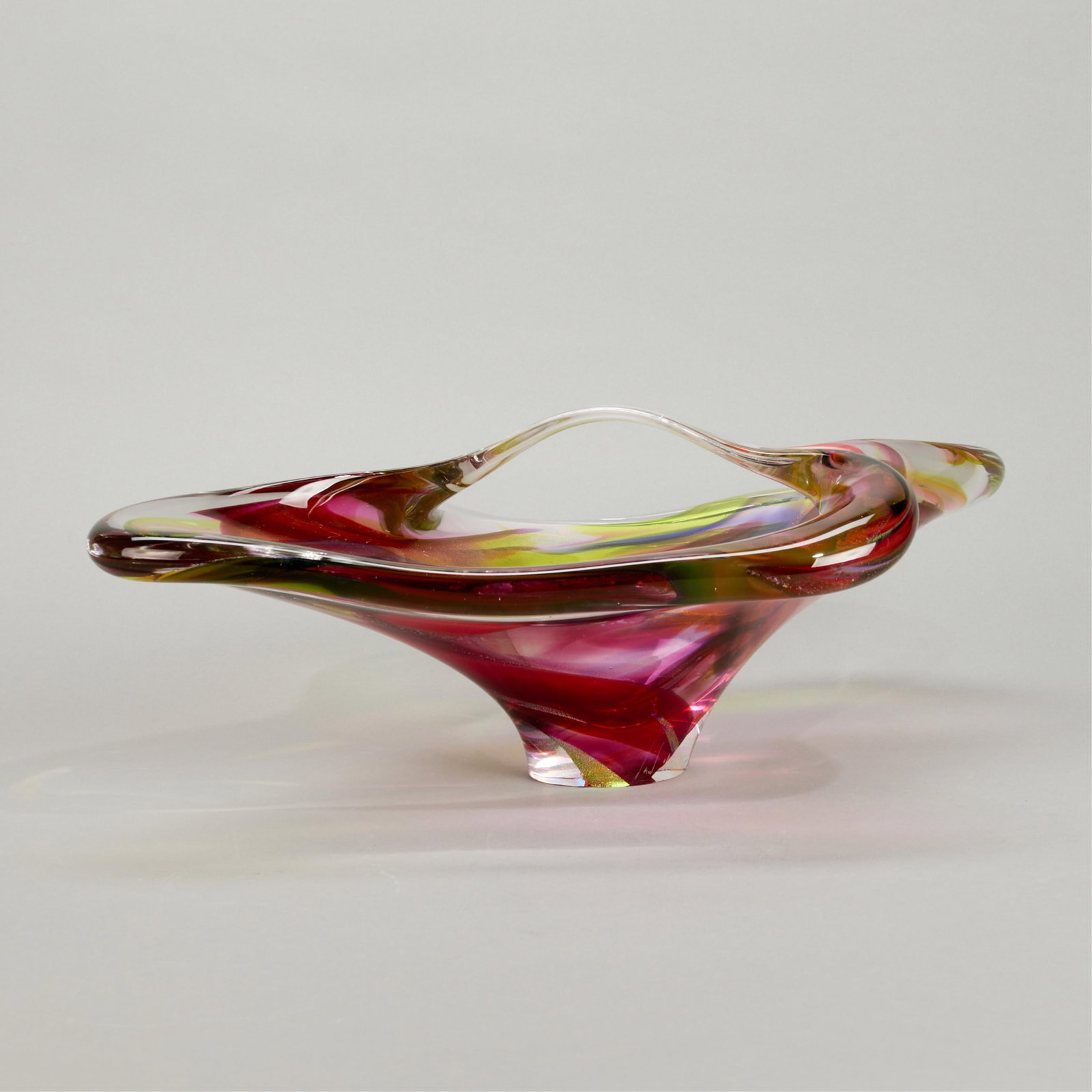 Modern Studio Art Glass Bowl 2007: Modern studio art glass handled bowl or basket, 2007. Of bright magenta glass with iridescent accents. Incised indistinct signature and dated along the footrim. Height: 8 in x width: 20 in x depth: 13