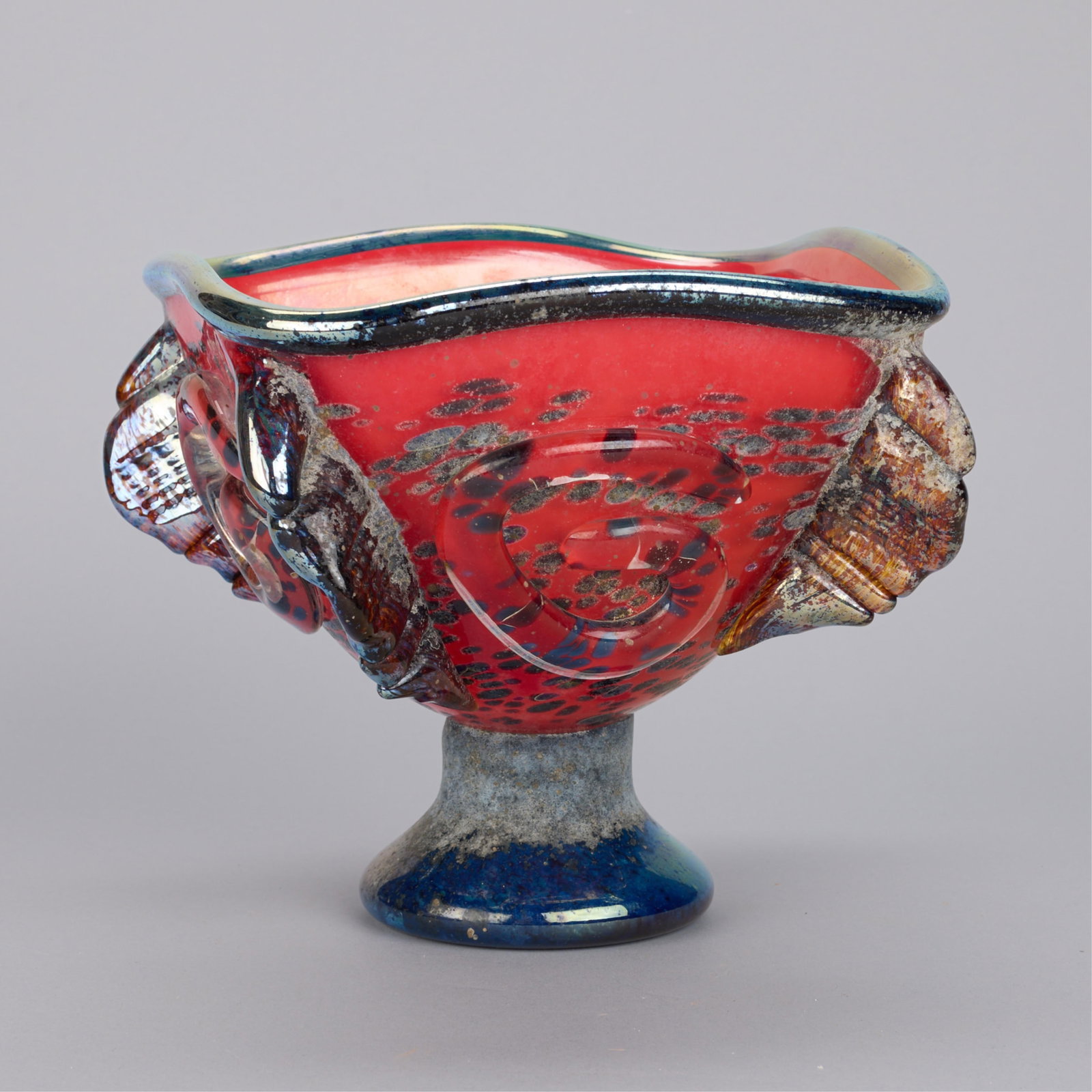Signed Red Art Glass Footed Bowl: Abstract art glass pedestal bowl with molded swirling and ruffled elements, 2002. Incised illegible signature and dated on the underside of the base. Height: 7 3/4 in x width: 8 in x depth: 8 in.