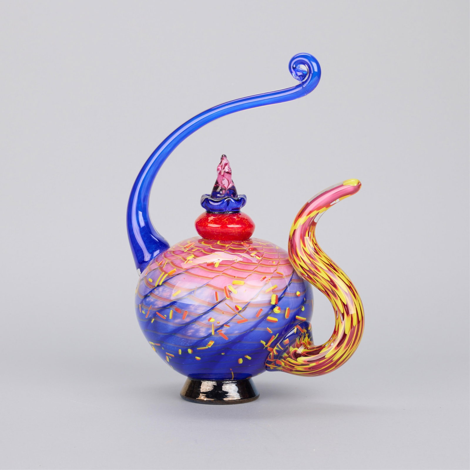 Christian Thirion Whimsical Glass Teapot Sculpture: Christian Thirion (American, 20th/21st century). Blown glass sculpture in the form of a whimsical teapot. Executed in blue, pink, yellow, and red glass. Incised signature along the underside. Height: 