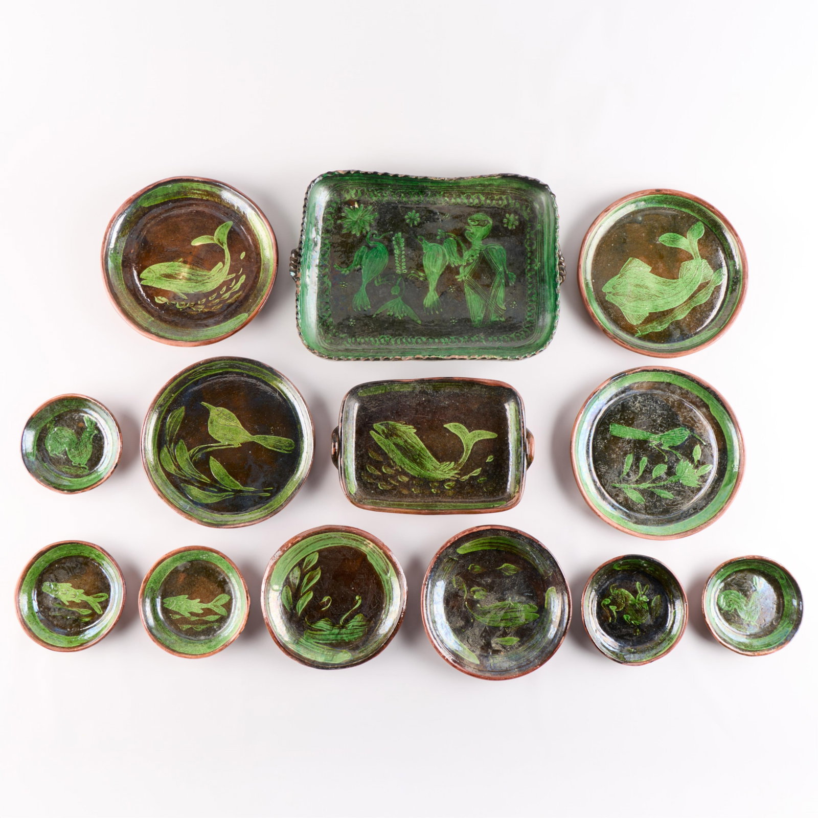 12 Pcs Mexican Tlaquepaque/Patamban Pottery Dishes: Set of 12 pieces of Mexican folk art "Tlaquepaque" or "Patamban" green-on-black tourist pottery dishes, 20th century. Each depicting fish, wildlife, and foliage. Including two two-handled rectangular 