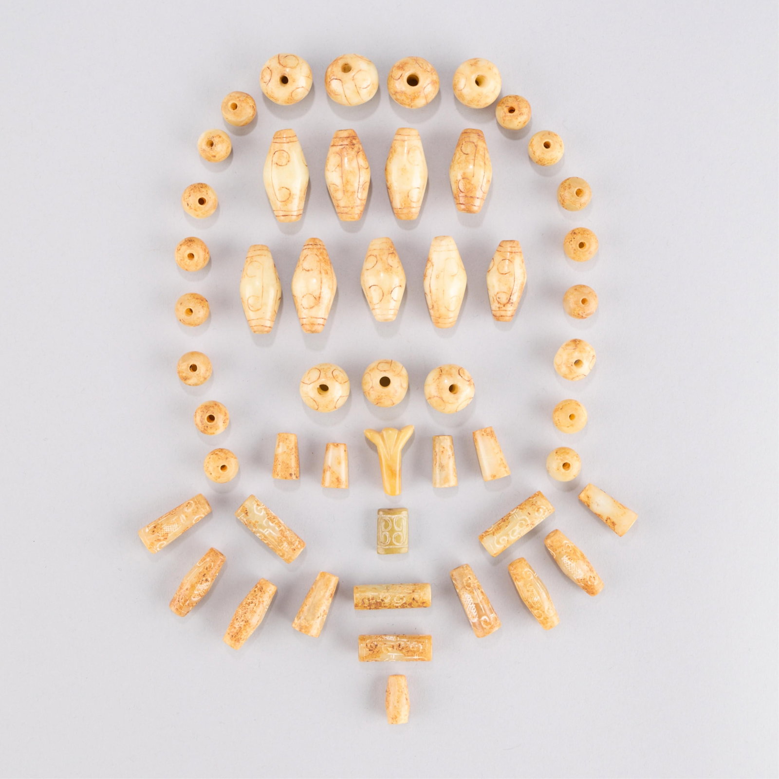 53 Chinese Jadeite Beads: Collection of 53 Chinese jade or jadeite carved beads. Each carved with C-form and geometric motifs. Of varying form. Gross weight of lot: 228.4 g.