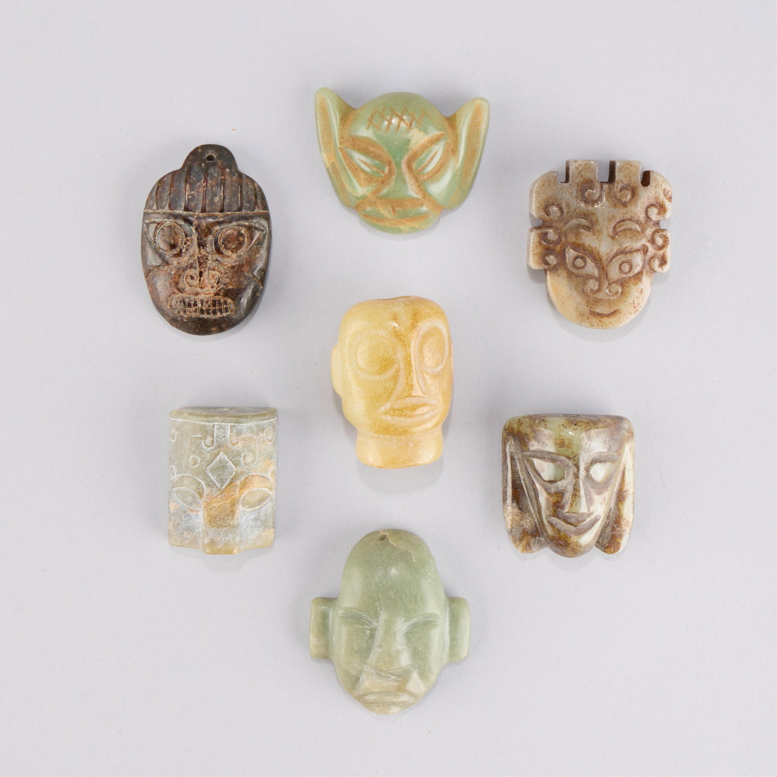 7 Chinese Jadeite Mask Carvings: Group of seven Chinese jade or jadeite carvings in the form of masks, taotie, or heads. Archaistic style. Height ranges from 1 1/2 in to 2 1/8 in; width ranges from 1 1/4 in to 2 in; depth ranges from