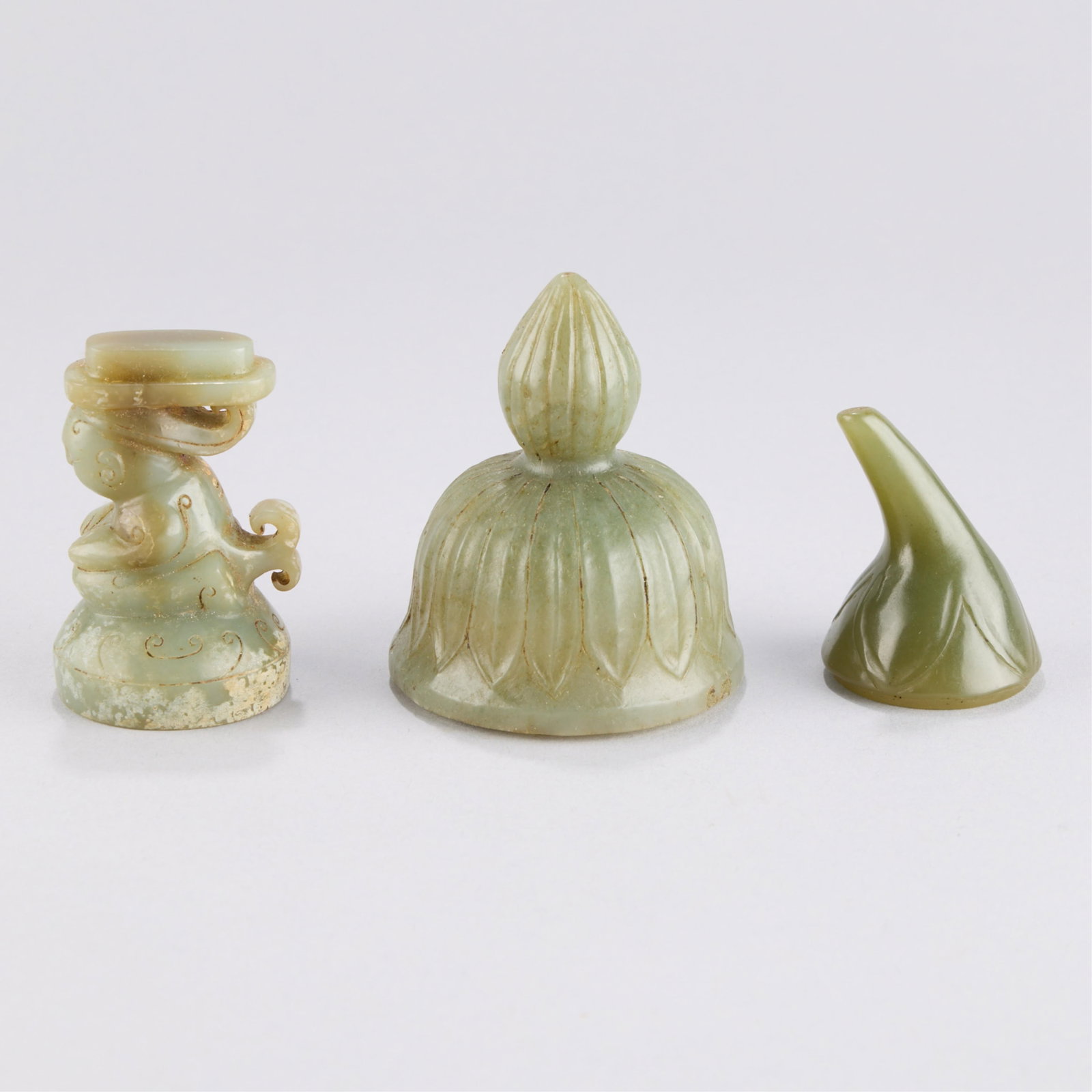 3 Chinese Jadeite Lids: Group of three Chinese carved jade or jadeite lids. On in the form of a gourd or plant top; one in the form of a crouched figure or merman/mermaid; and one with incised petal motifs. Height ranges
