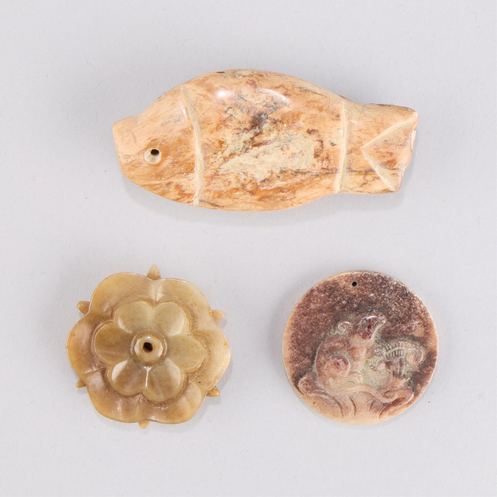 3 Chinese Carved Jadeite Pendants: Group of three Chinese carved jade or jadeite pendants. One in the form of a fish; one in the form of a lotus blossom; one carved with an incised rat next to a lingzhi mushroom. Height ranges from 1
