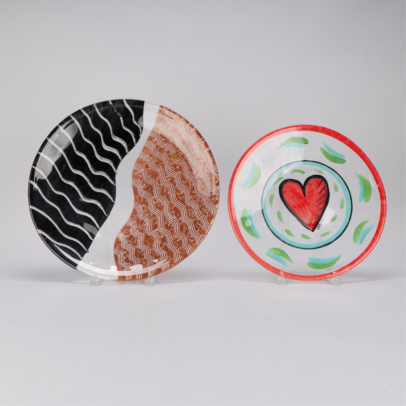 2 Kosta Boda Glass Platters: Group of two painted Kosta Boda glass platters. Including one plate designed by Ulrica Hydman Vallien from the "Friendship Hearts" series and a second plate designed by Monica Backstrom from the "Tong