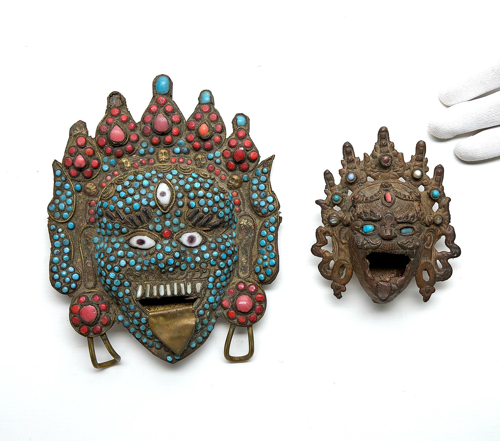 2 Antique Tibetan Inlaid Brass Mahakala Masks: Group of two antique Tibetan inlaid brass Mahakala masks, votives, or incense burners. Each with inlaid turquoise, coral, and other stones. The smaller mask resting on a tripod base. (Smaller) Height: