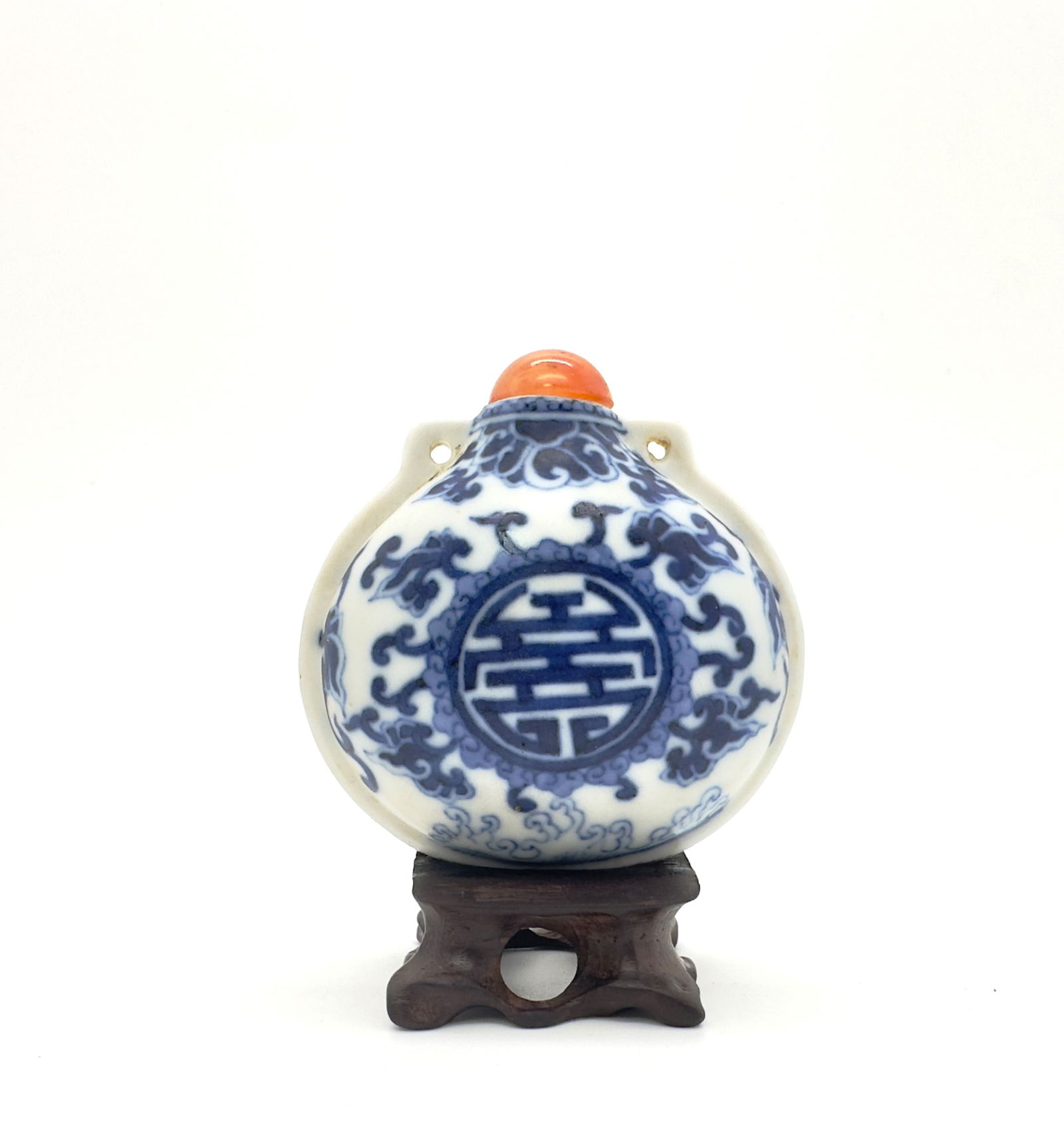 A Chinese Blue and White Porcelain Pouch-Form Snuff Bottle: beautifully molded in the form of a small pouch with angular shoulders pierced as loops flanking the neck, decorated with shou medallions and lotus sprays above crashing waves; carved coral stopper.He