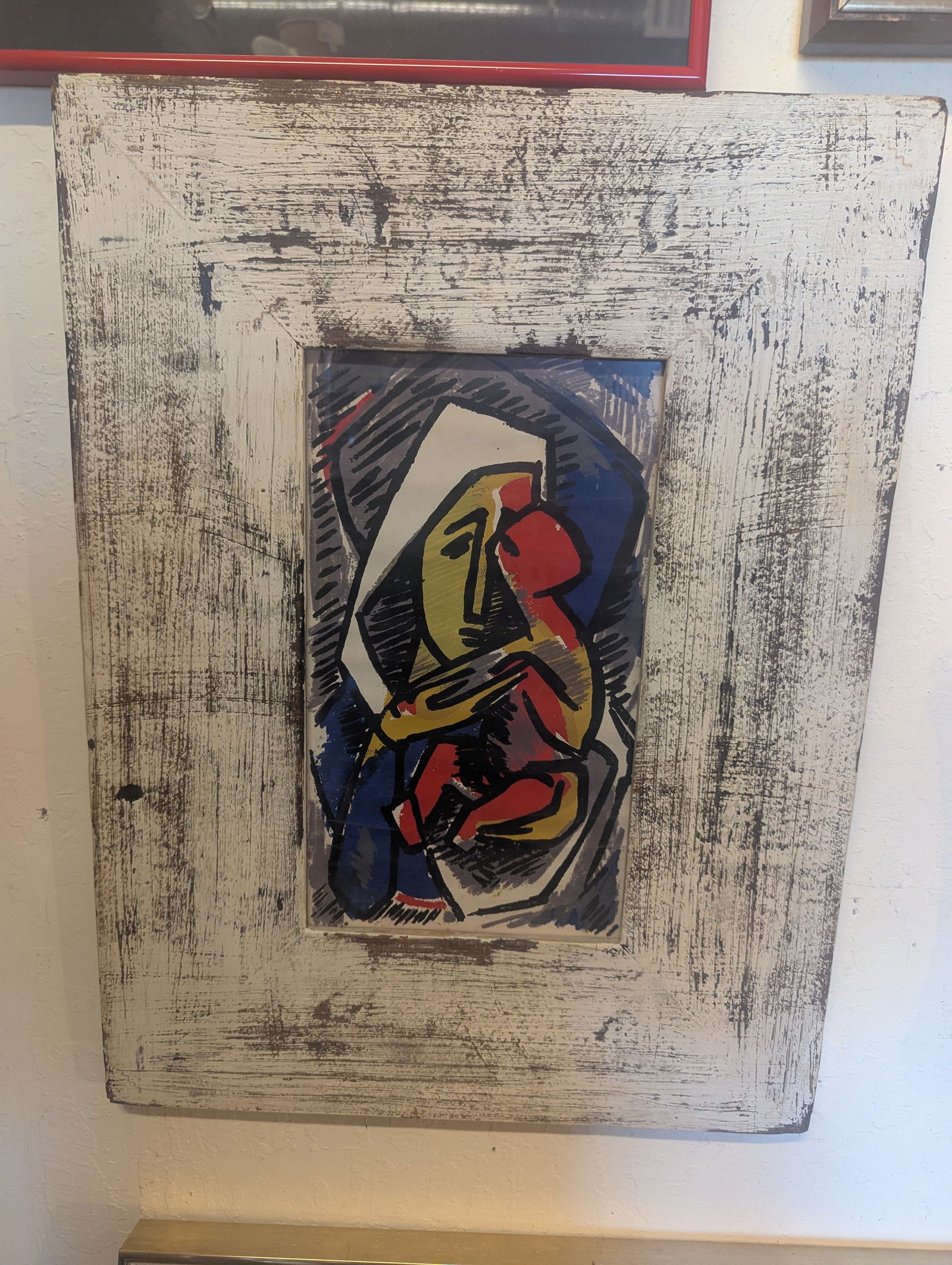 A collectible framed stylized art: A collectible framed art piece titled Quete Des Origines by Haitian artist Philippe Dodard. It features stylized, abstract figures in red, yellow, and blue housed in a rustic, weathered white fram,