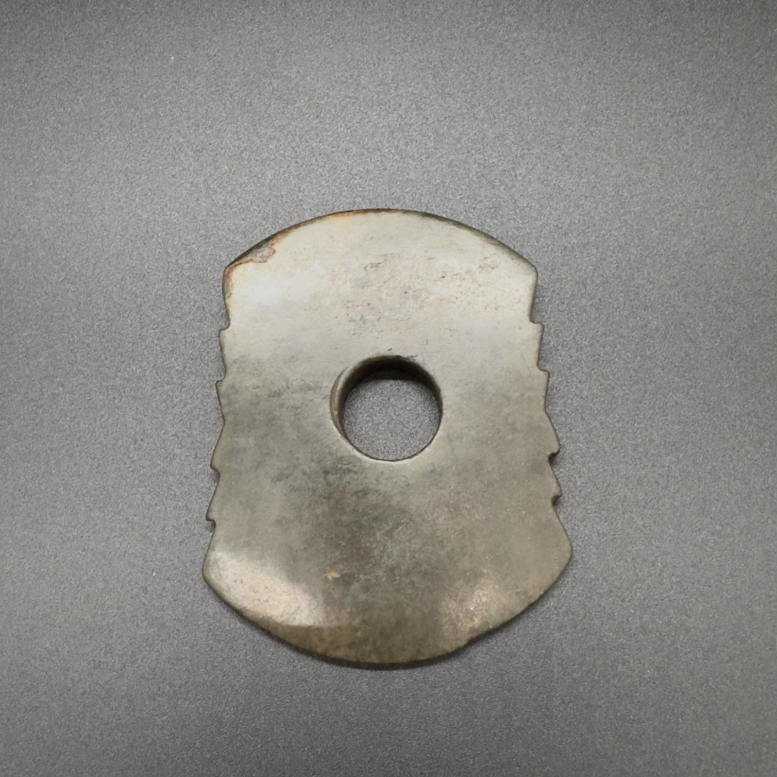 A Chinese Jade Axe, (475-221 BC): This jade implement takes the form of a ceremonial axe , with a broad, rounded blade and a central circular aperture for mounting. The sides are adorned with symmetrical stepped notches, a hallmark of