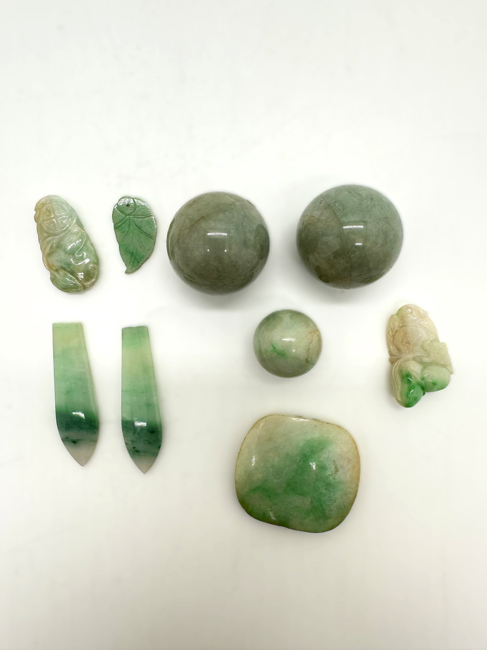 Group of Chinese Jadeite Carvings and Beads,19th.C: This group of jadeite objects showcases a variety of forms and uses, all carved from translucent jadeite with natural green and white inclusions. The set includes:Two carved animal toggles (likely dep
