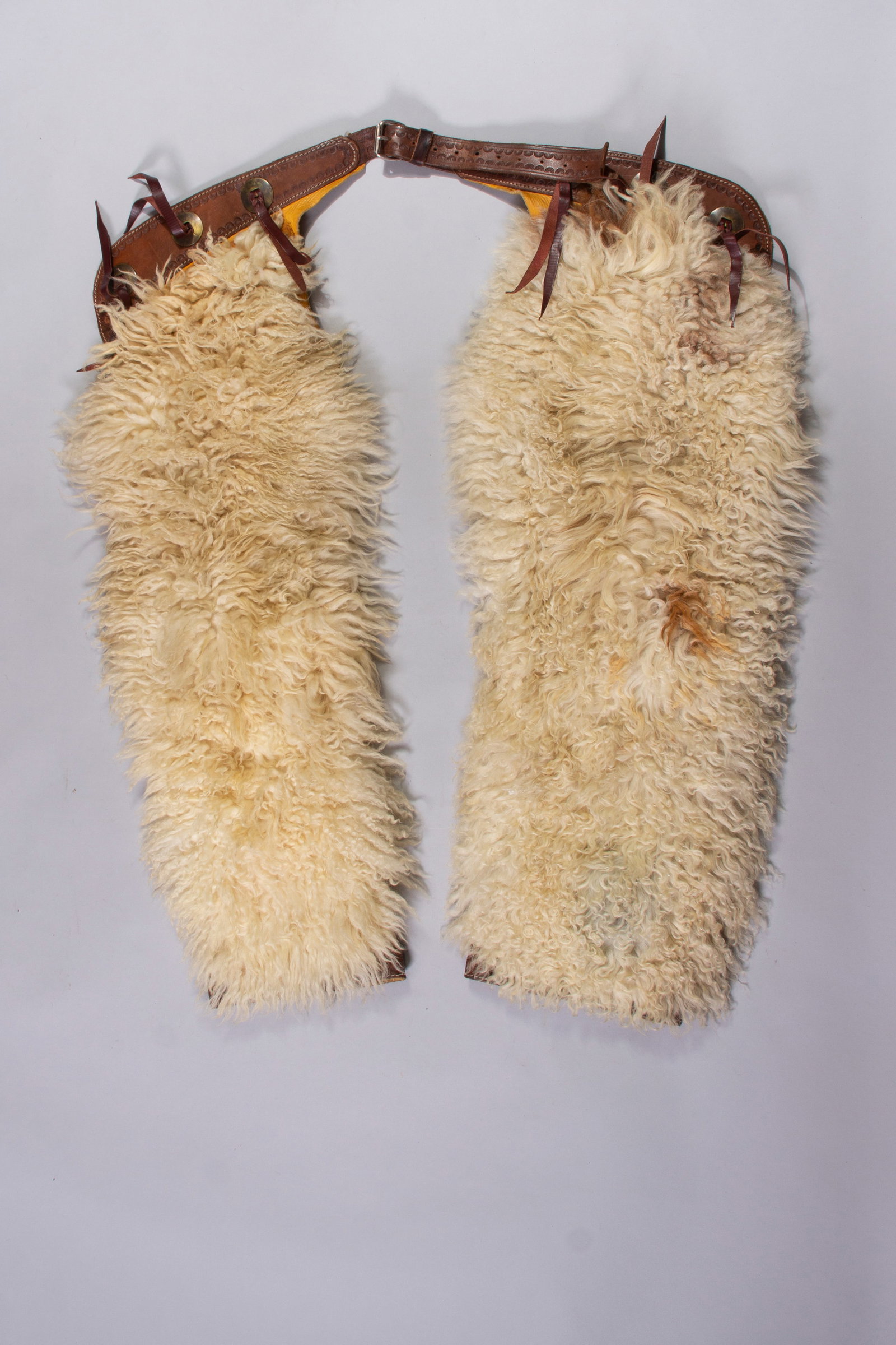 White Wooly Chaps Unmarked: White Wooly Chaps Unmarked on hide with 3 slotted conchos on each side of belt. Additional sunburst tooling along belt. Length: 38"