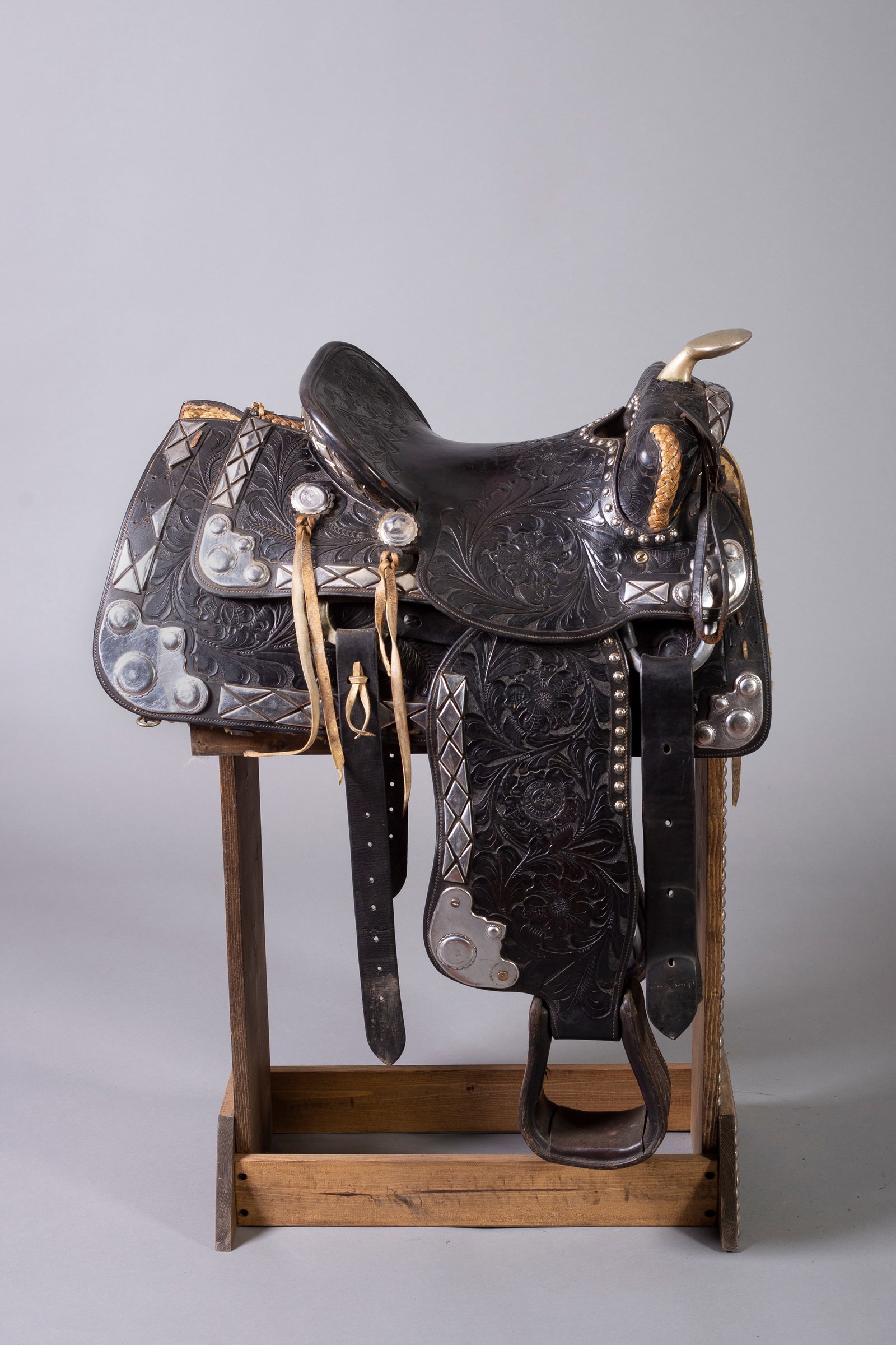 Black Saddle with Silver Accents Marked Monroe Veach, Trenton MO: Black fully tooled saddle with silver accents and conchos with braided pommel and grey strings. Marked Monroe Veach, Trenton MO on seat. Custom stand included.
