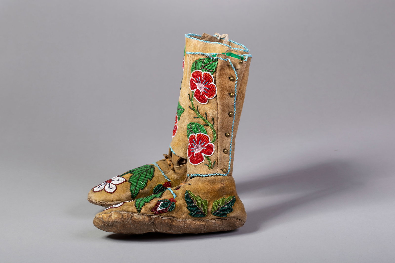 Nez Perce High Top Floral Design Beaded Moccasins: Nez Perce High Top floral design beaded Moccasins; Thread sewn, in green, red, white, brown, navy, light blue and silver beads. Brass buttons on outside on uppers and light blue beaded trim. Measureme