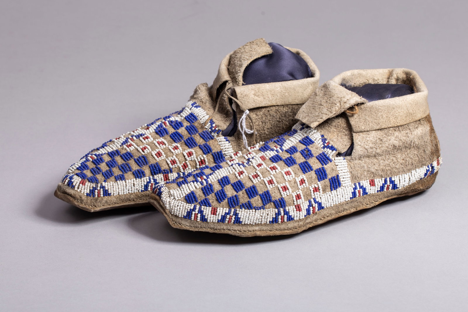 Sioux Moccasins, Ca.19th Century, Fenn Family Collection: Sioux Moccasins, Ca. 19th Century. Checkered vamp in navy, white and pumpkin beads with white around edge and middle with geometric designs. Measurement: 9 3/4"L, Provenance: Previous owner of the Thr