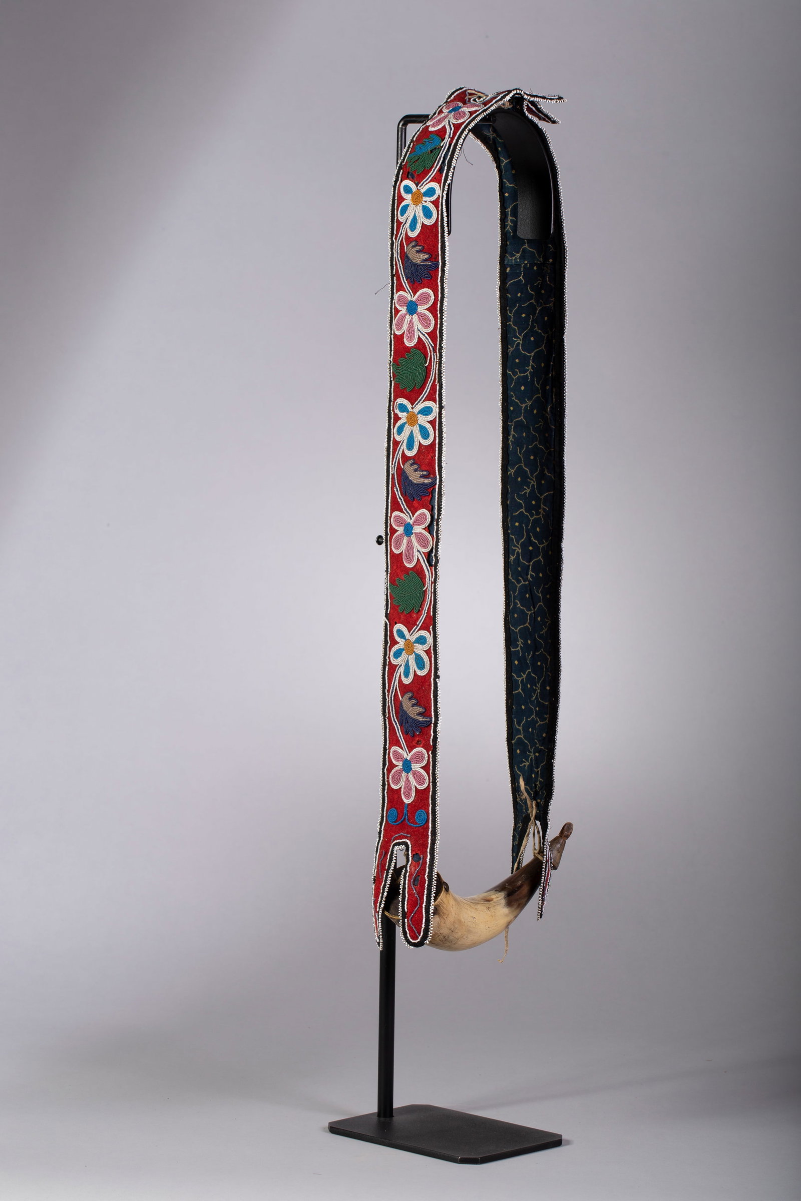 Powder Horn, Cree Beaded Floral Sling: Thread sewn red trade wool with navy trim and backed with navy trade cloth. Beaded abstract floral design in colors of white, green, aqua blue, translucent periwinkle and pink straps with tacked powde