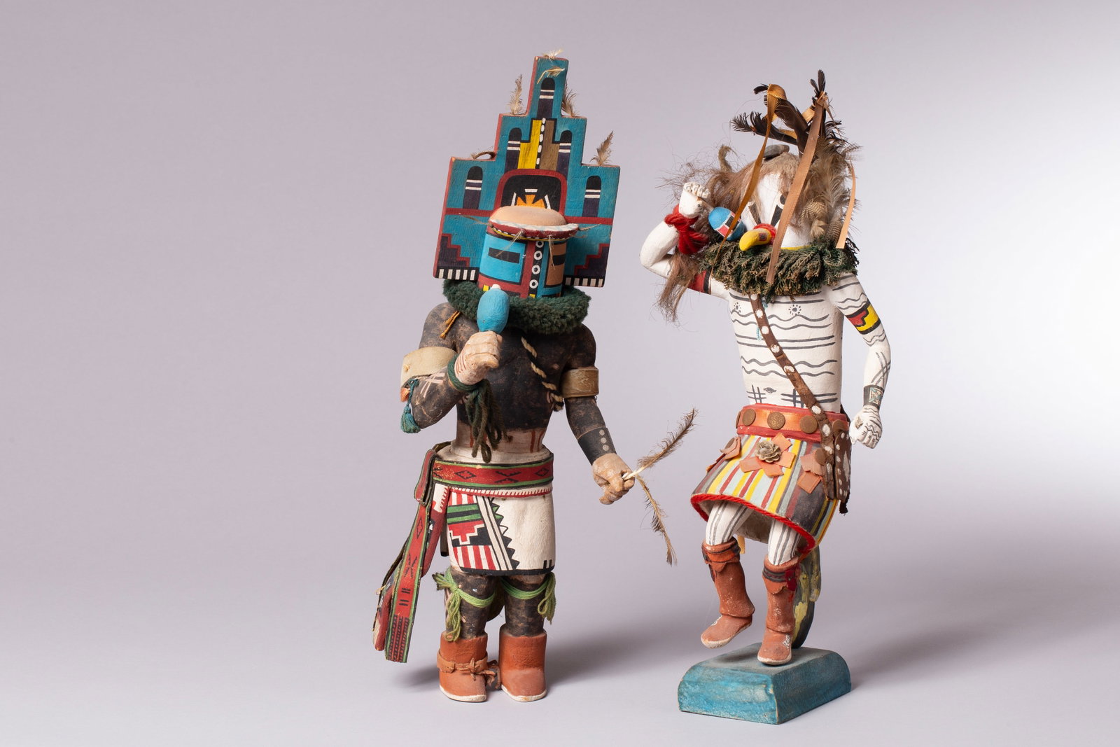 Lot of 2 Kachina Dolls: 1) Depicting a Hopi Tunei-nili, or "Small River Katsina" doll, made from carved cottonwood root, polychrome painted, featuring a yellow beak and feathers atop the head. He appears at summer katsina da
