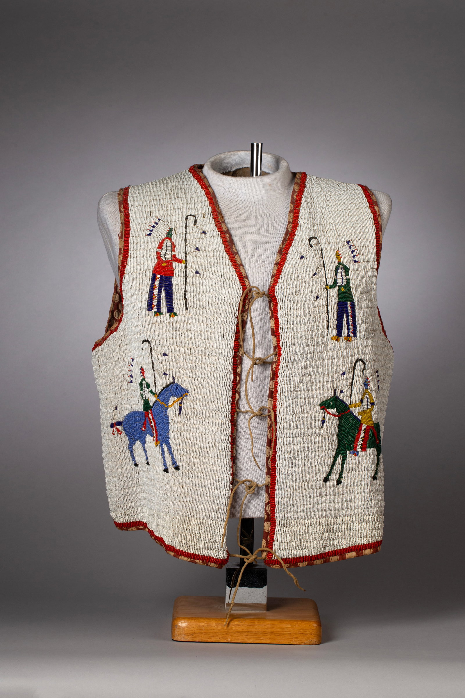 Sioux Fully Beaded Vest depicted with Horseriders: A striking pictoral with 8 Sioux warriors, in full dress. Four of the figures are on horseback and four are standing. Beaded in a white background with warriors beaded in multi color, inside lining in