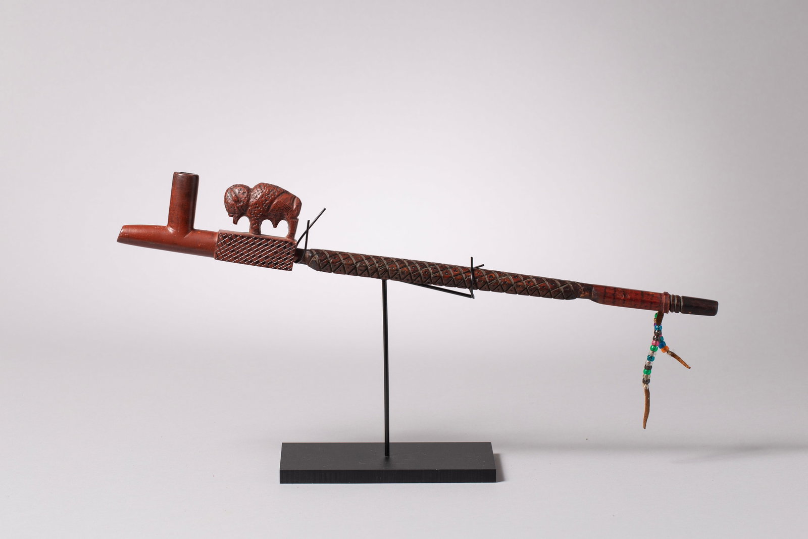 Plains Catlinite Pipe with Buffalo Effigy: Featuring a carved buffalo on the pipe block, the bowl is joined to a deeply carved wooden stem, decorated with crosshatched diamond patterns