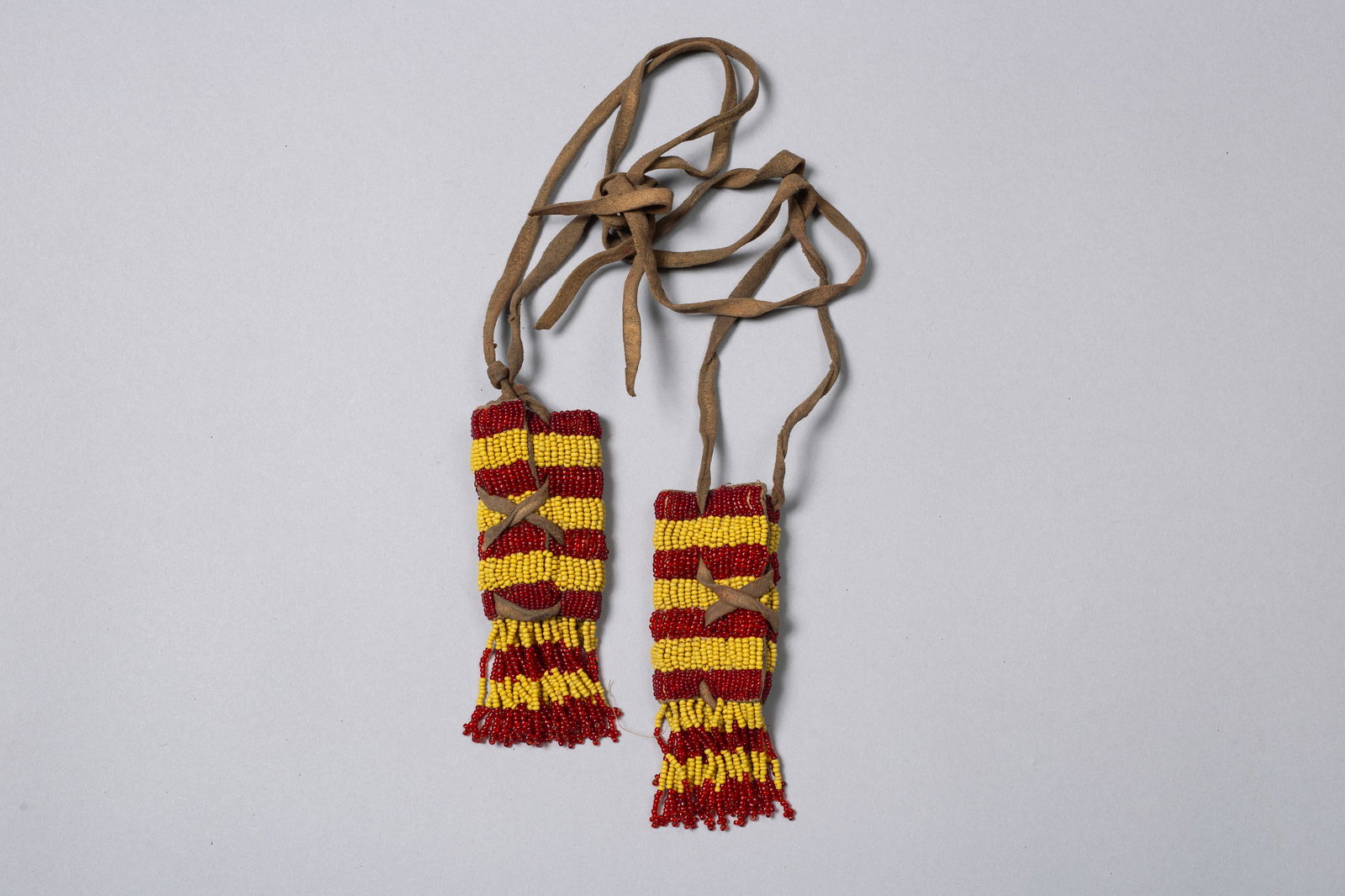 Pair of Beaded Hair Braid Drops: Each with bright red and yellow striped glass seed beads over a rawhide strip, 4 1/4" Length including fringe, 1 1/2" Width, leather strips that braid into hair approximately 14" long