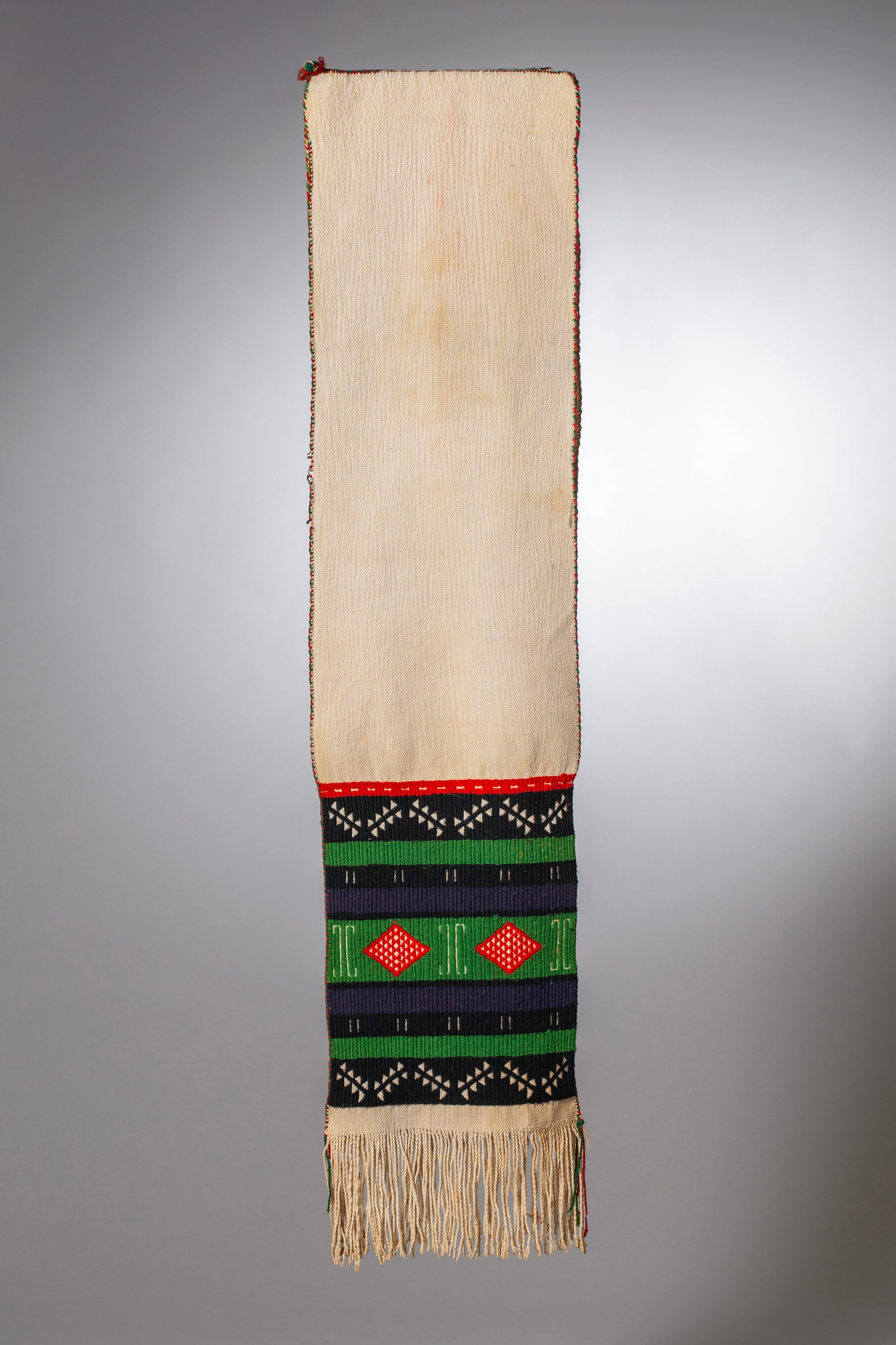 Native American Vintage Hopi Ceremonial Dance Sash: Woven in soft white cotton with plied fringe, the ends decorated with woven geometric bands in red, green, and black, featuring diamond and stepped motifs, 99" total (48 1/2" each half including fring