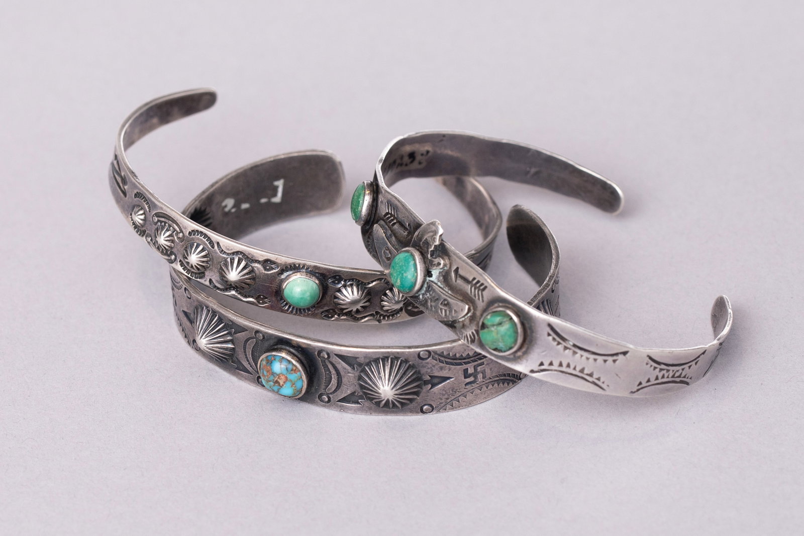 Lot of 3: Vintage Fred Harvey Era Coin Silver Petite Bracelets with Storyteller Bands: All stamped sterling silver1) Adorned with a small turquoise stone, whirling logs, and arrows, Ca. 1930s 5" Internal Circumference, 1 1/8" Gap, 1/2" Width17 grams2) Adorned with woman in a canoe, 3 sm