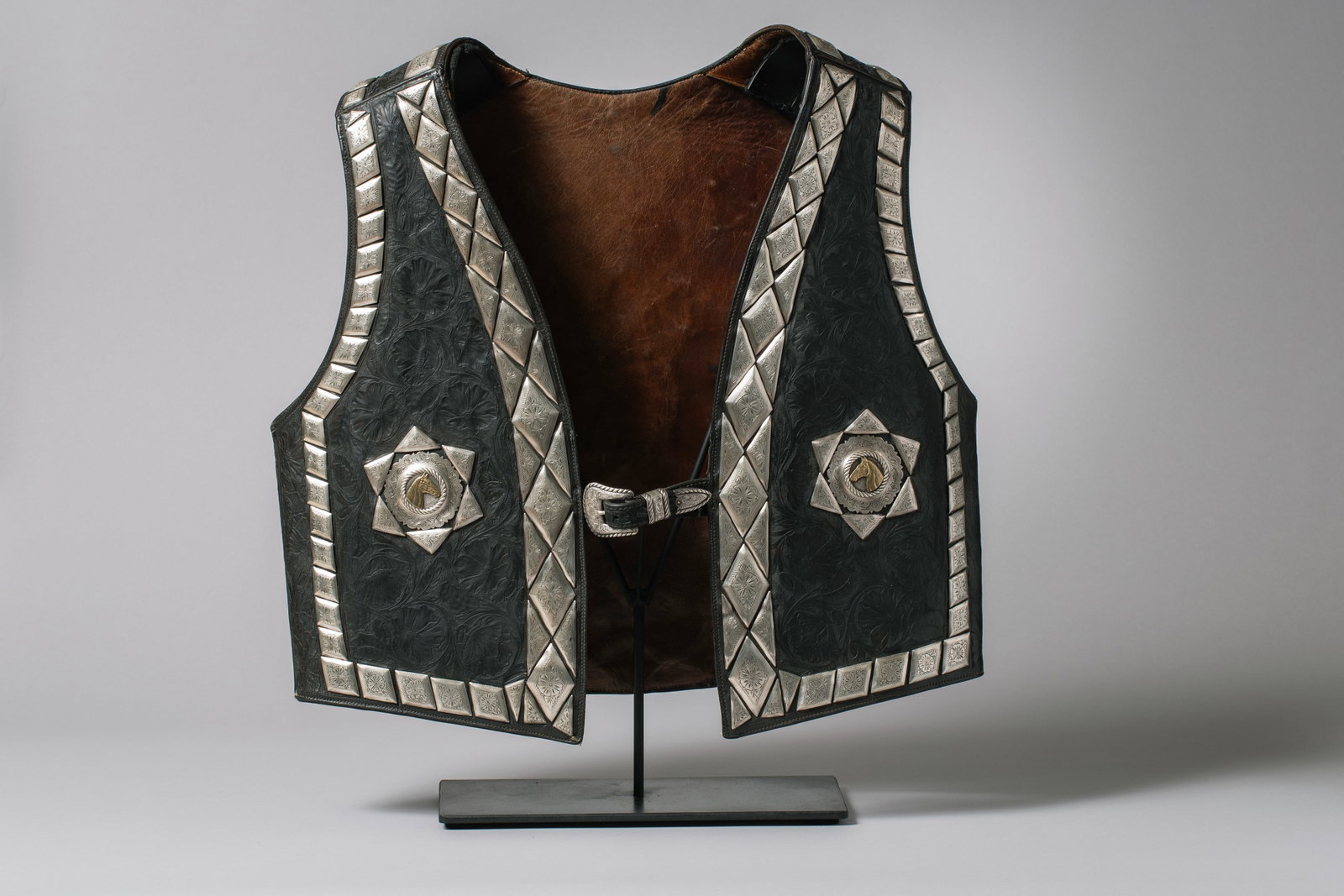 Vintage Western Black Vest adorn with Sterling Silver Diamond and Brass Horseheads in Conchos: This beautiful 1940s Black Western vest with floral tooling, sterling silver engraved diamonds, engraved silver conchos with gold horseheads, brown leather lining with an engraved buckle marked "sterl