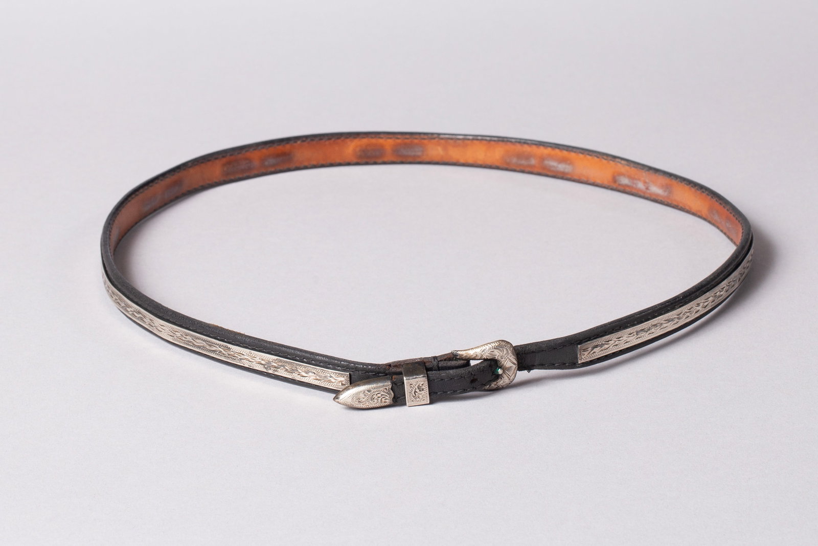 Edward H. Bohlin Black Leather Hat Band with Sterling Silver engraving: Marked "Bohlin" and "Sterling" on buckle and "Bohlin Made" on tip. Black leather band with engraved overlaid silver band. Total length 25 3/4"