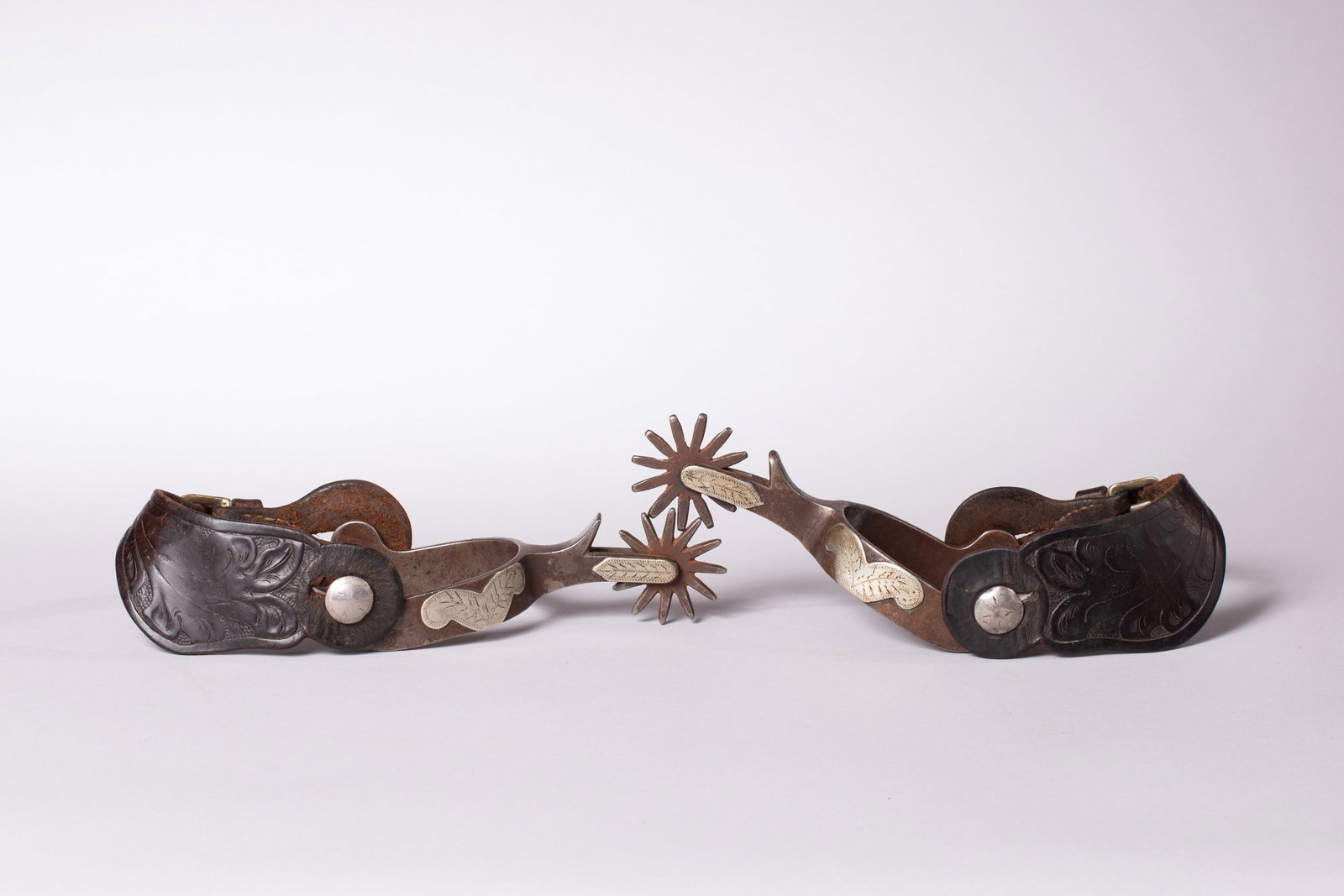 Crockett Mustache Pattern Spurs: Marked "CROCKETT" near button, single mounted, overlay engraved silver on heel band and shank with nice old floral tooled straps. Heel band opening 3 1/4", Heel width 1", Shank 2 1/2"L, 12-point rowel