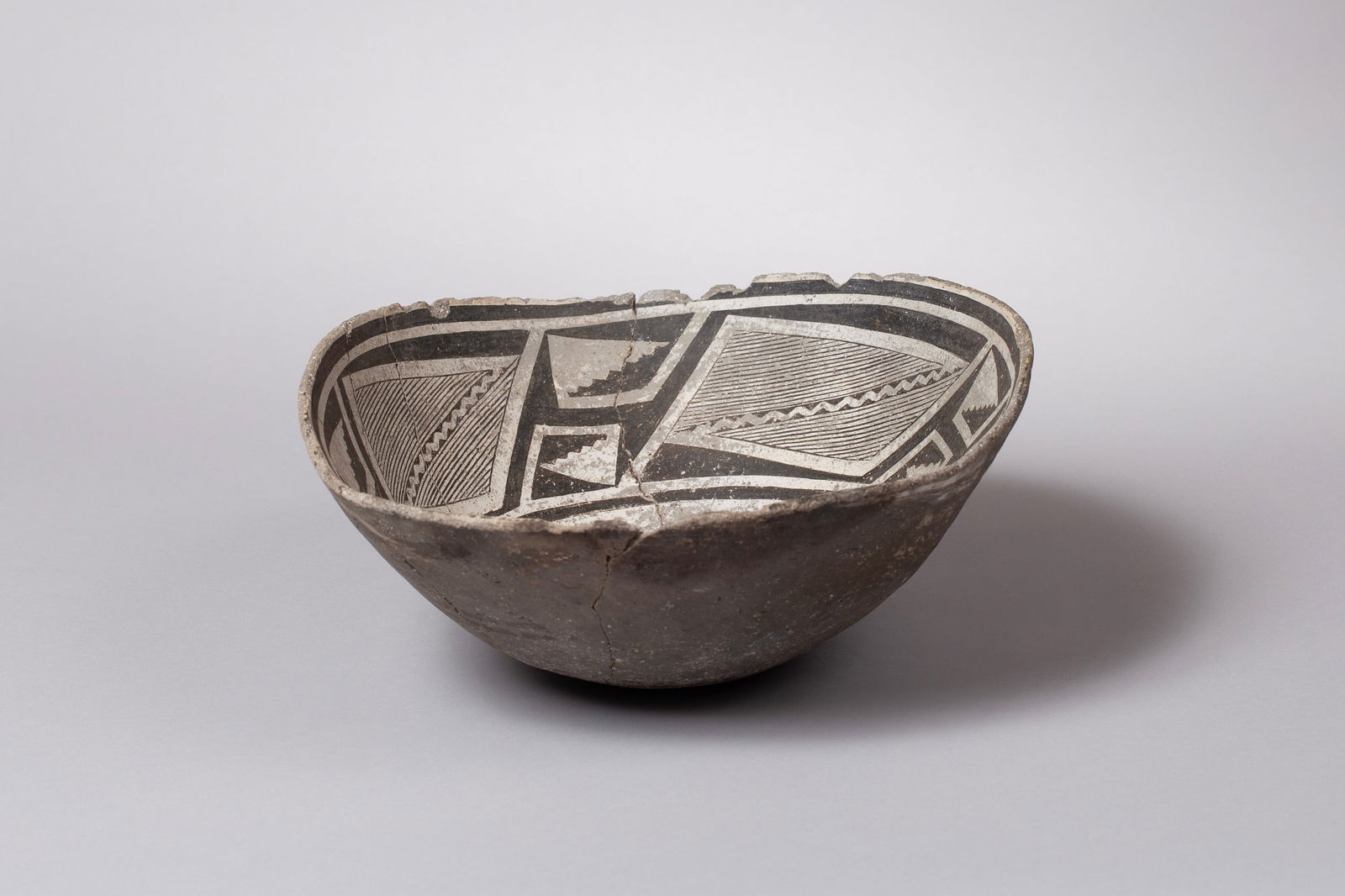 Classic Mimbres Black-on-White Geometric Bowl, Ca 1000 - 1130 AD: A Classic Mimbres black-on-white bowl, ca. 1000–1130 AD, decorated with a distinct and finely painted geometric design on the interior. The bowl exhibits a slight oval shape, a testament to its hand
