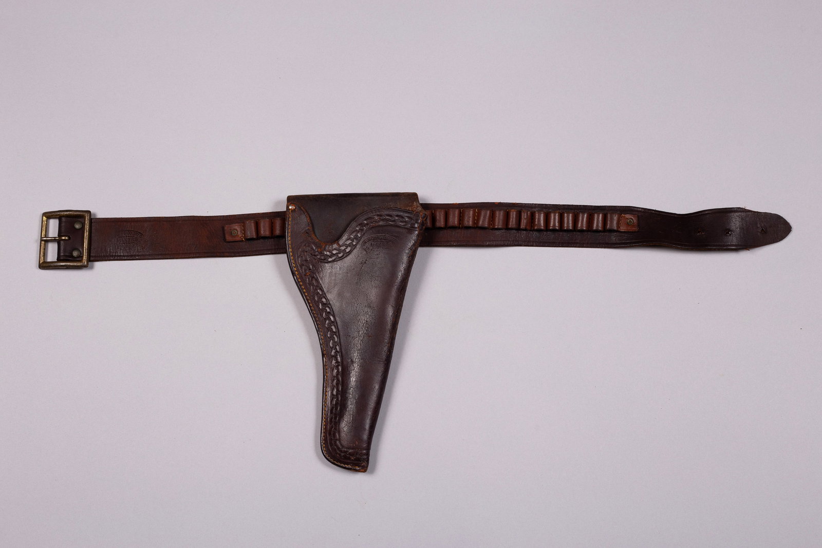 Miles City Gun Rig: A nice marked "Miles City, Saddlery Co." cartridge belt and holster. Holster has weave border tooling. Belt holds 26 cartridges. Holster length 11". Belt length 29 1/4".