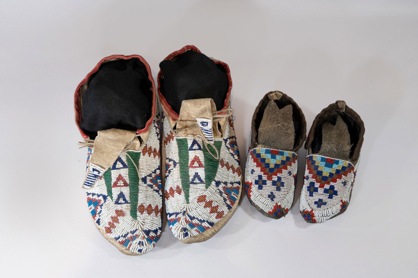 Two pair of Sioux Beaded Moccasins, 1880-90s: Two pair of bead Sioux moccasins: 1. Adult size, trade cloth trim and beaded in geometric designs, sinew sewn. 2. Kids size, beaded in geometric designs with heel fringe which is symbolic for wiping a