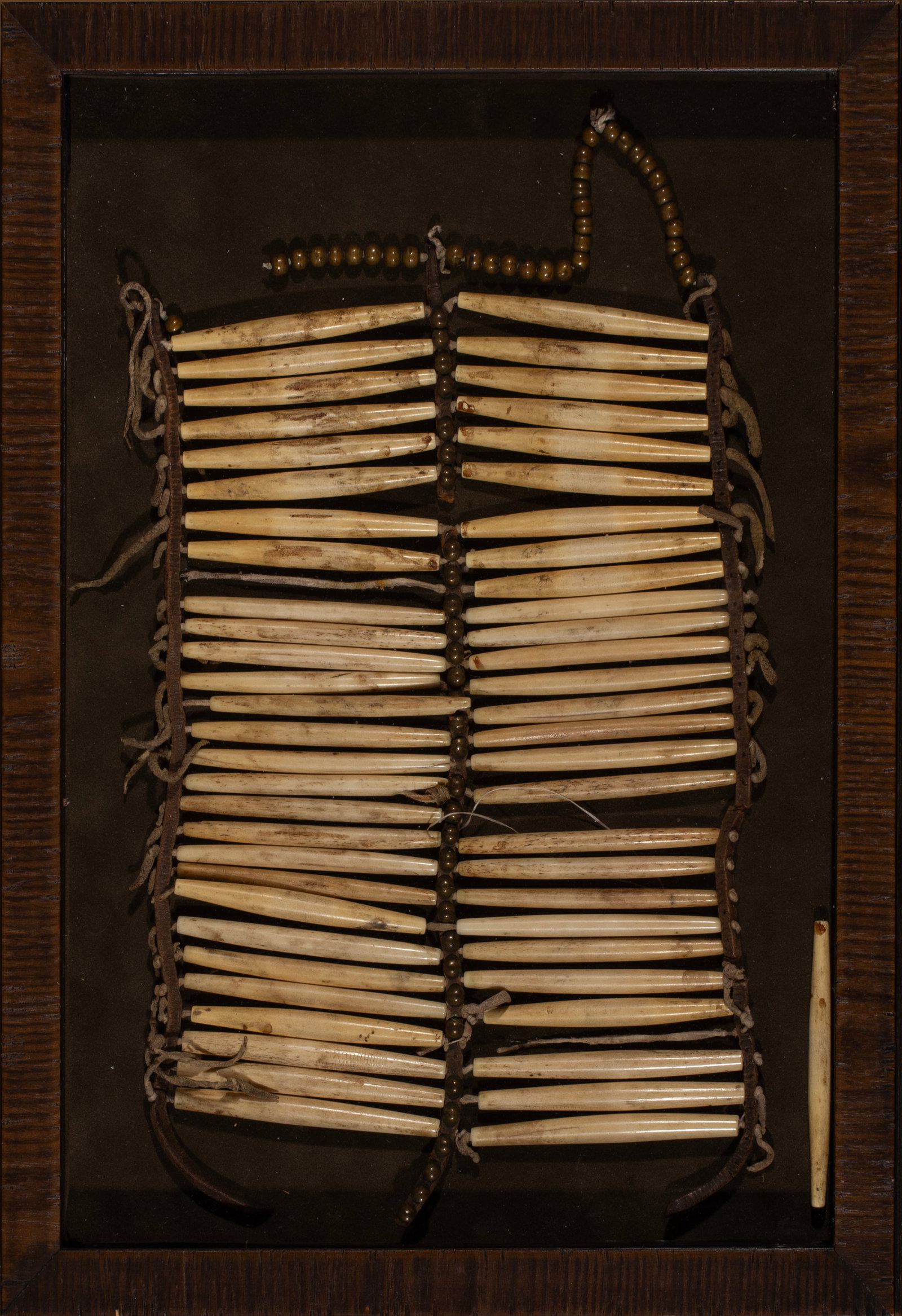 Northern Plains Breastplate in Shadowbox, Ca 1880-90s: Northern Plains bone tube breastplate. Two sections of bone pipe tubes accented with brass tacks through the middle and brass beads along the bottom. Fastened with old harness leather. In an attrative