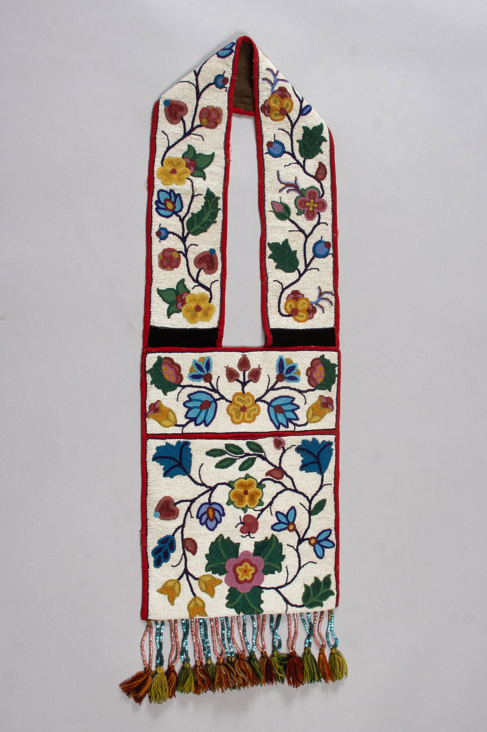 Great Lakes Area Bandolier Bag, Iroquois, c. 1890s: Great Lakes / Haudenosaunee (Iroquois) bandolier bag, circa 1890, finely executed in a white beaded ground with blue and green polychrome floral and foliate motifs in shades of blue, greasy pink, yell