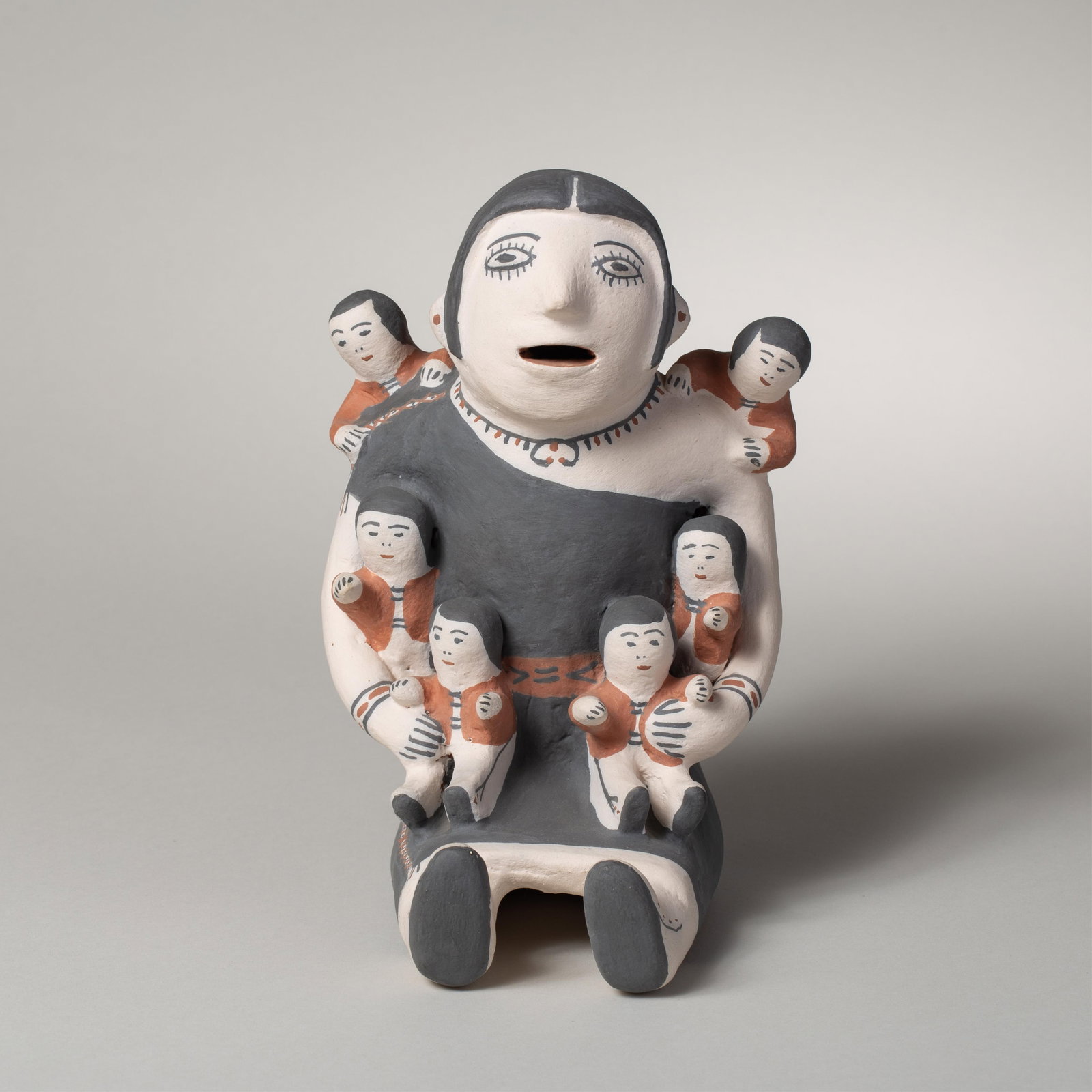 Felipa Trujillo, Storyteller: Felipa Trujillo pottery figure depicting a seated female holding multiple children, rendered in polychrome with a matte surface. The children are resting on the figure positioned at the shoulders,