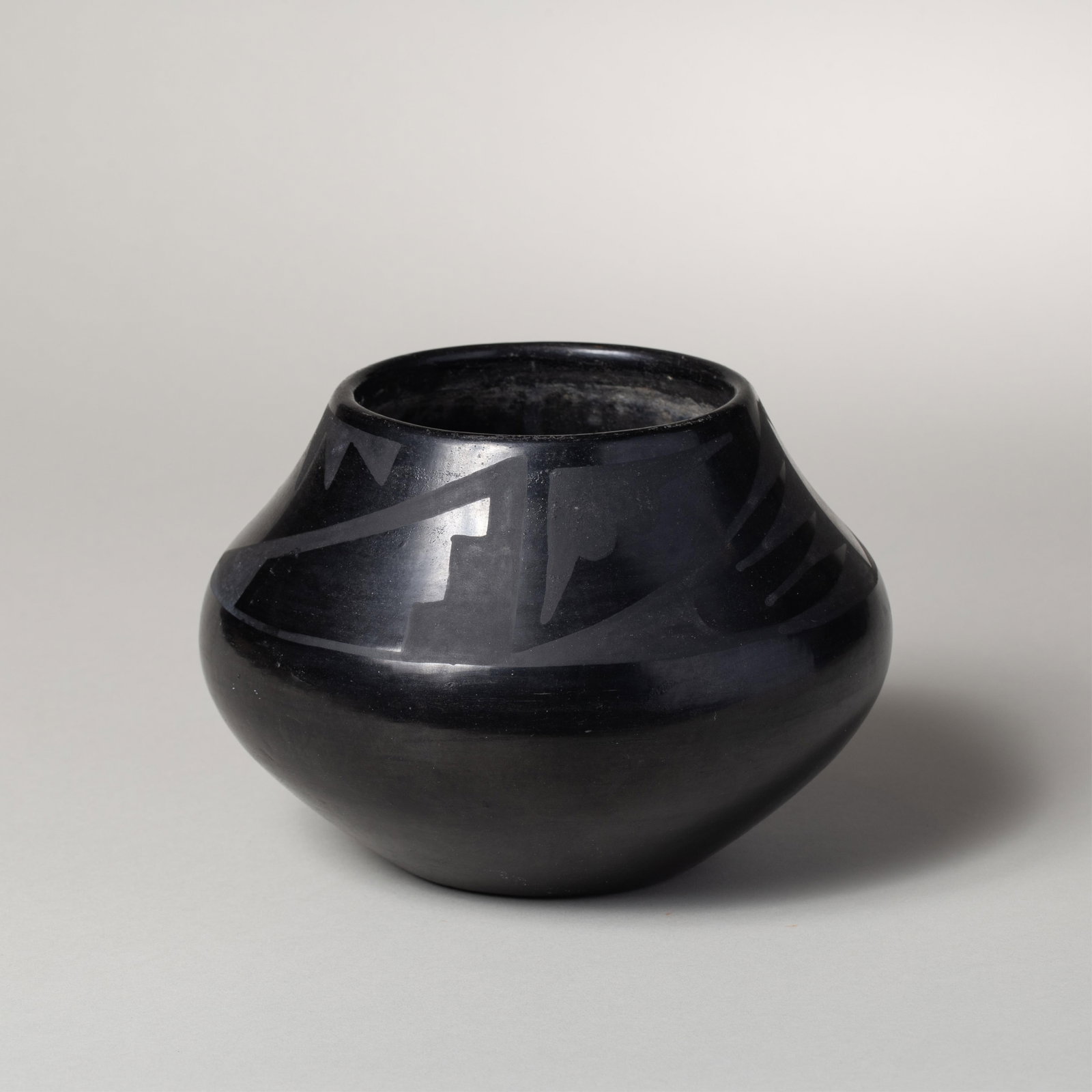 Maria & Santana Martinez, Avanyu Pot: Maria and Santana Martinez San Ildefonso blackware jar of low, wide-shouldered form, the highly polished surface bearing a matte avanyu design encircling the shoulder. The vessel is rendered in the tr